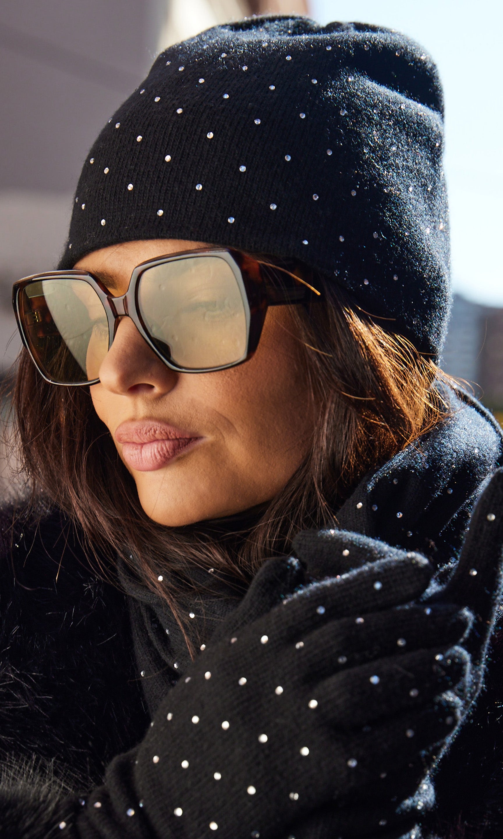 Person wearing a black beanie with white crystals, sunglasses, and gloves.