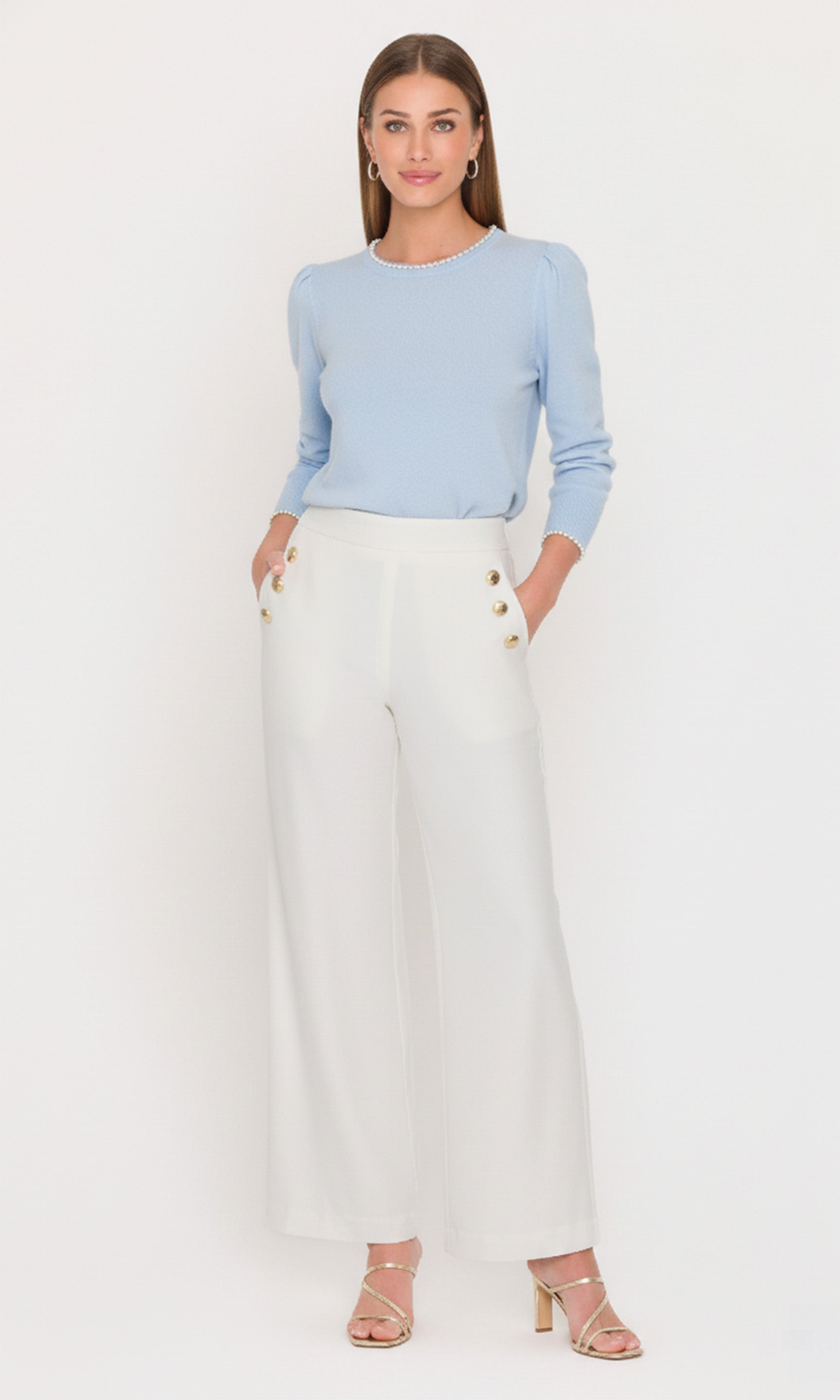 Woman wearing a light blue sweater and white pants on a white background