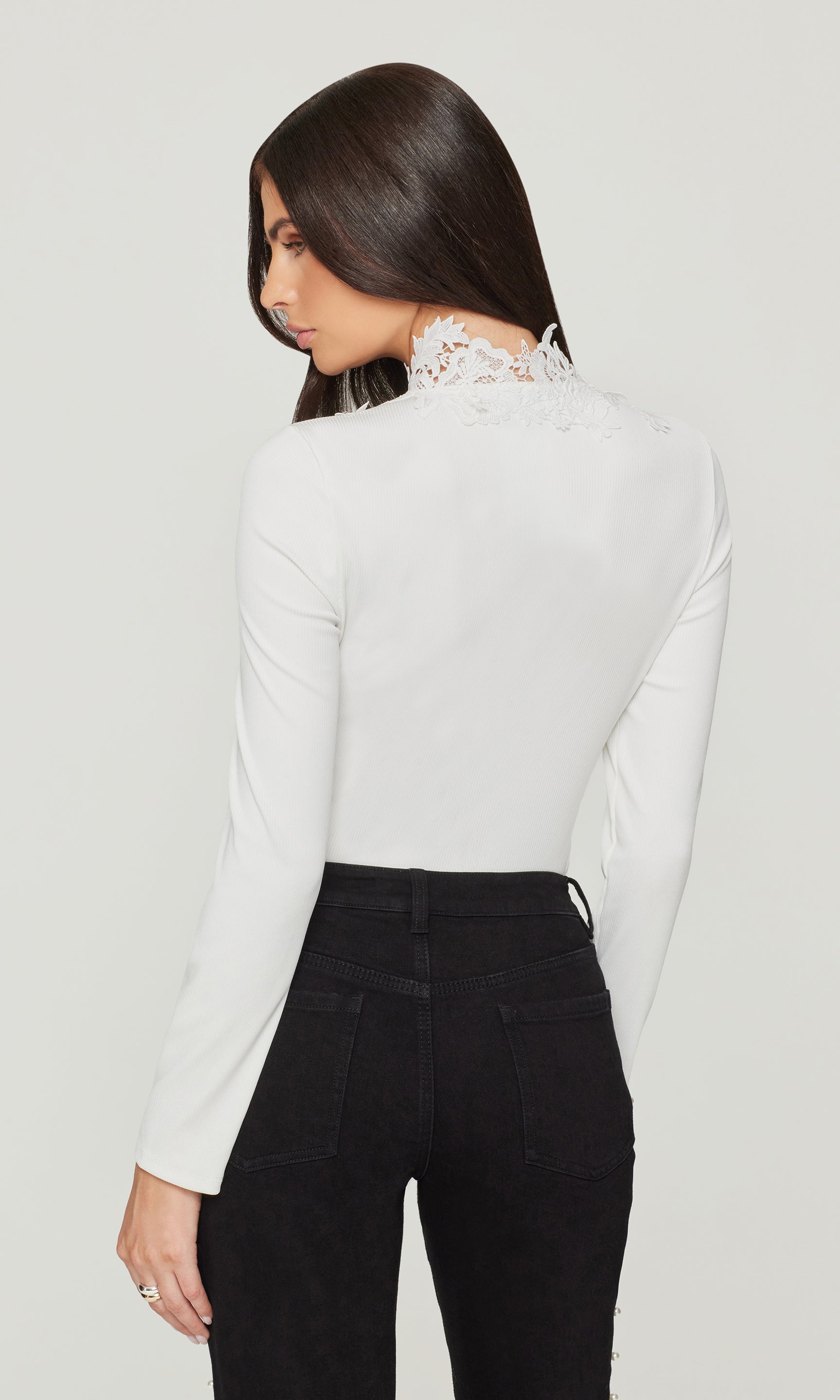 Woman wearing a white blouse with lace detailing and black pants on a plain background