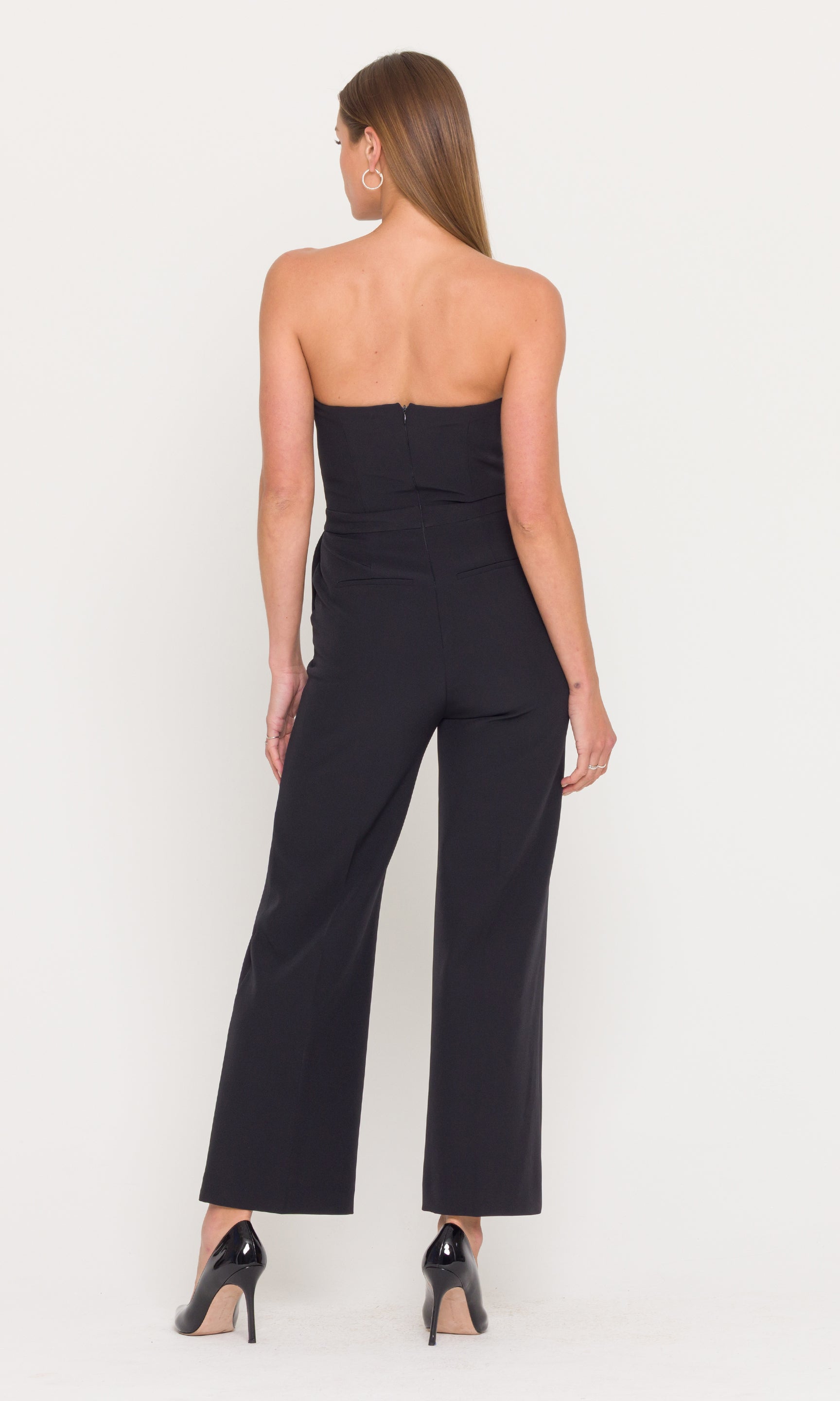 Back view of woman wearing a black strapless jumpsuit on a white background