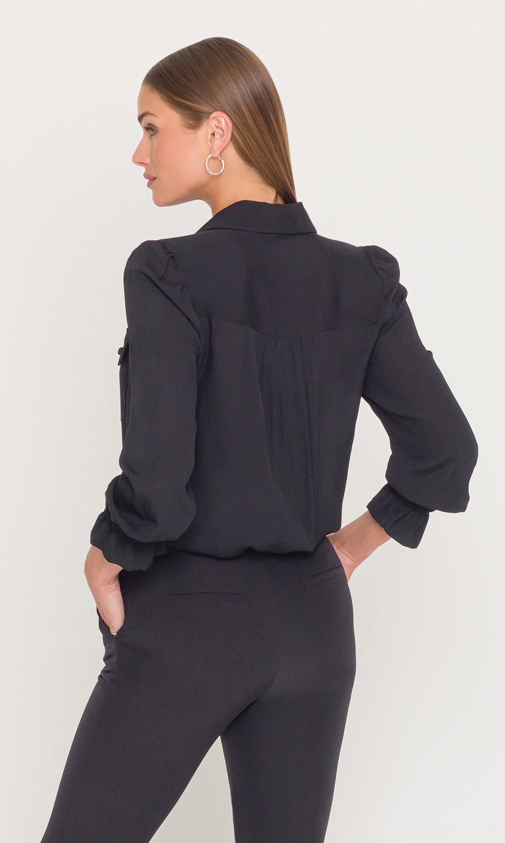 Back view of woman wearing a black outfit with a jacket and pants on a white background