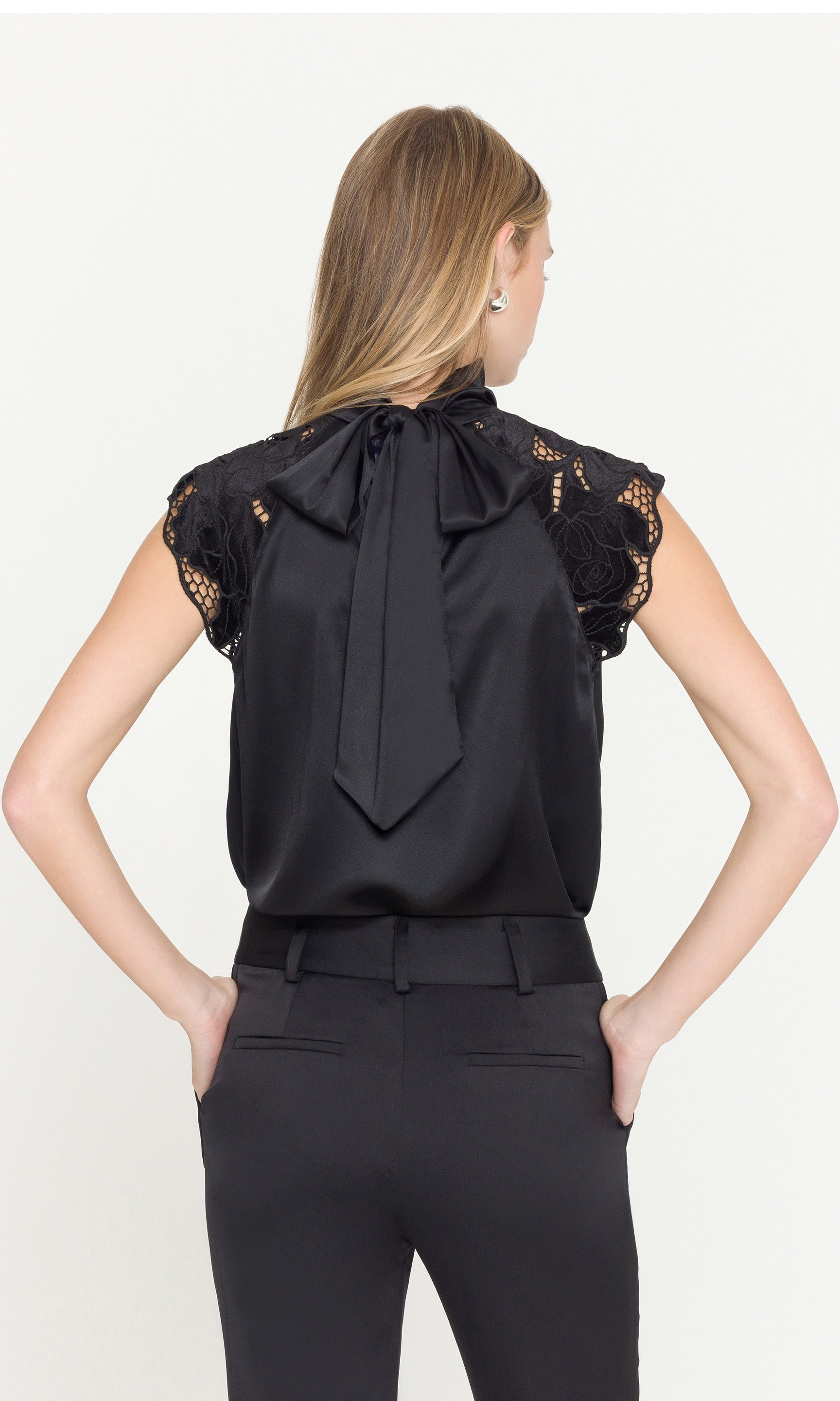 Black blouse with lace details on sleeves and tied back by a person on a white background