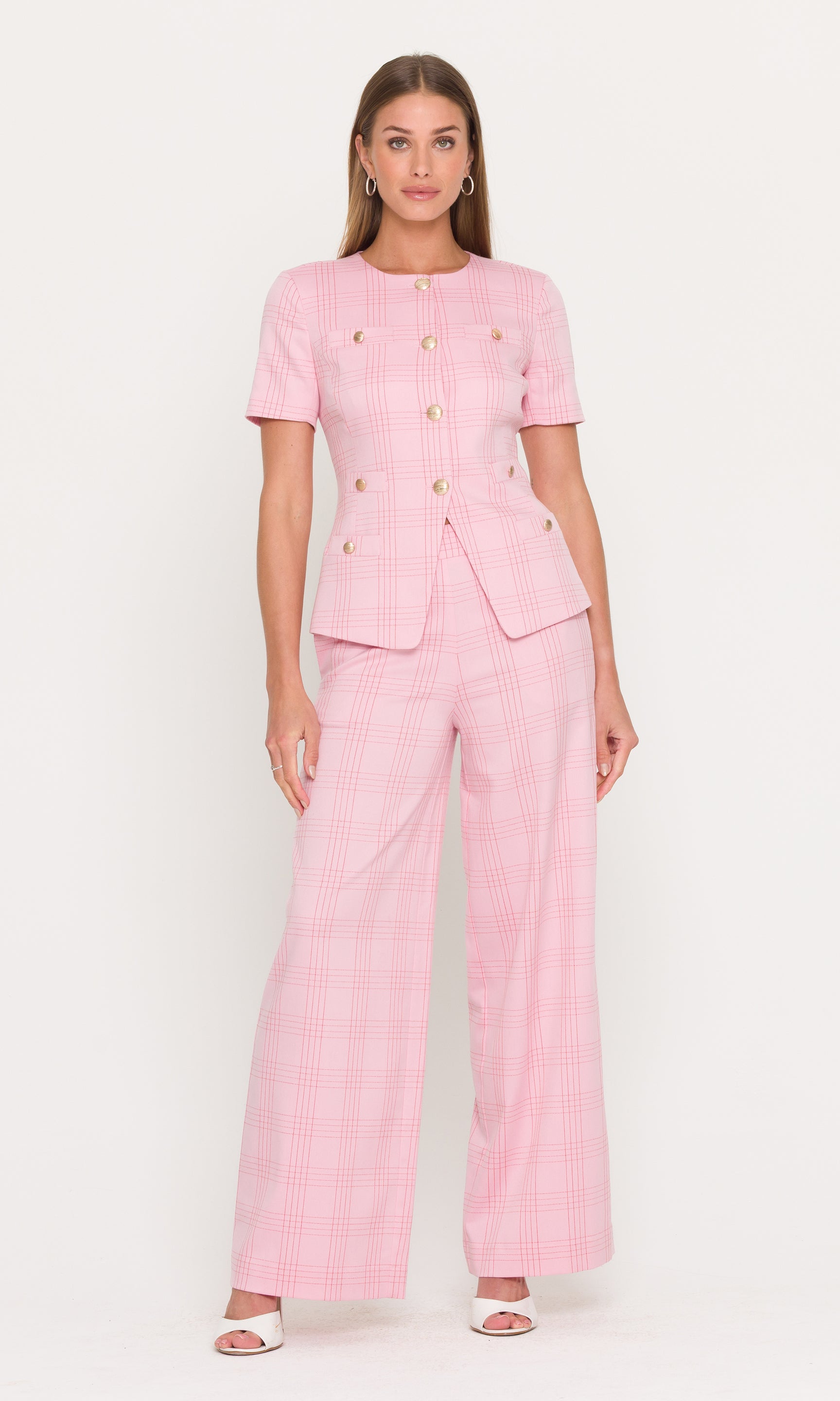 Full body image of woman wearing a pink suit with gold buttons on a white background