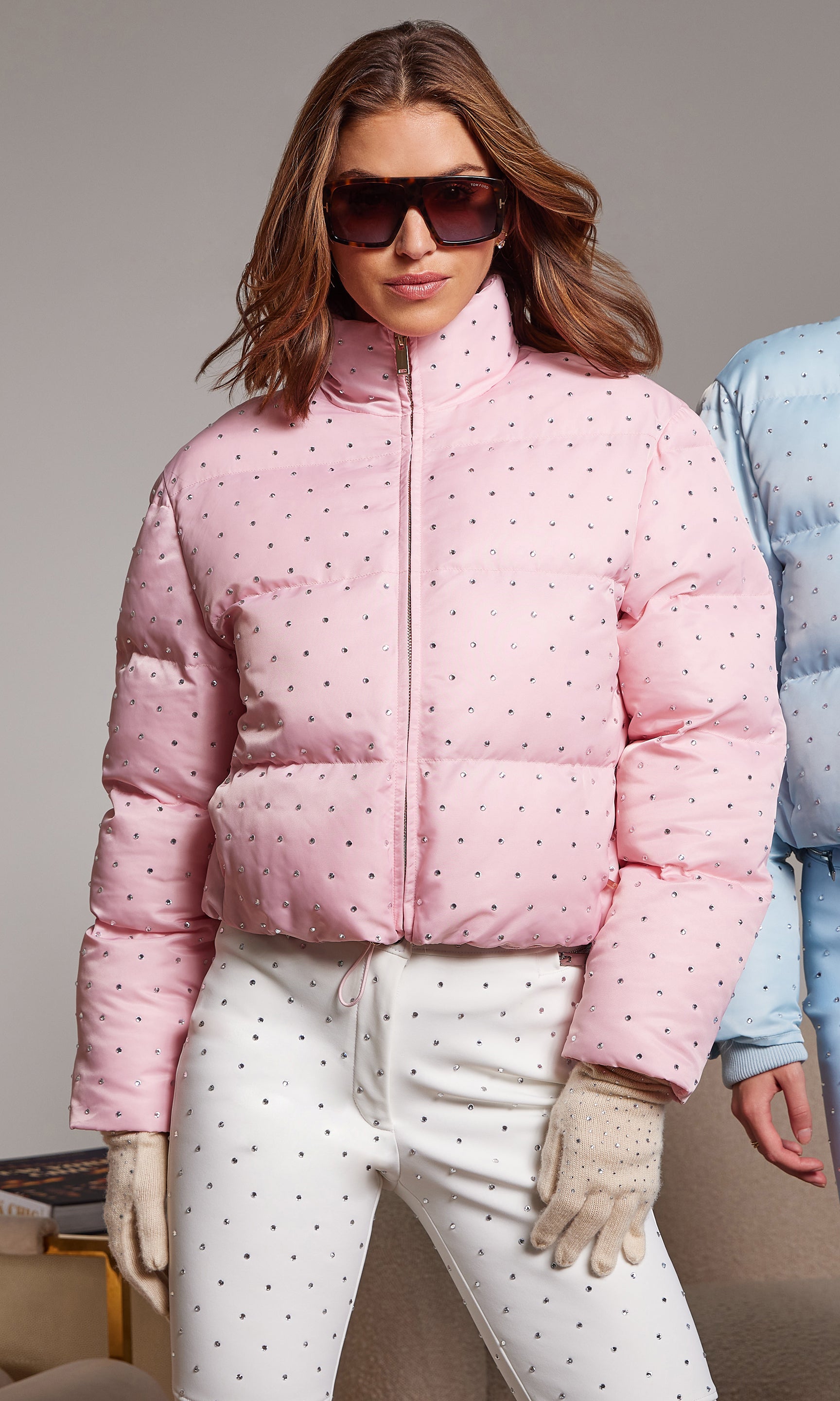 Woman wearing a pink crystal puffer jacket and sunglasses on a plain background