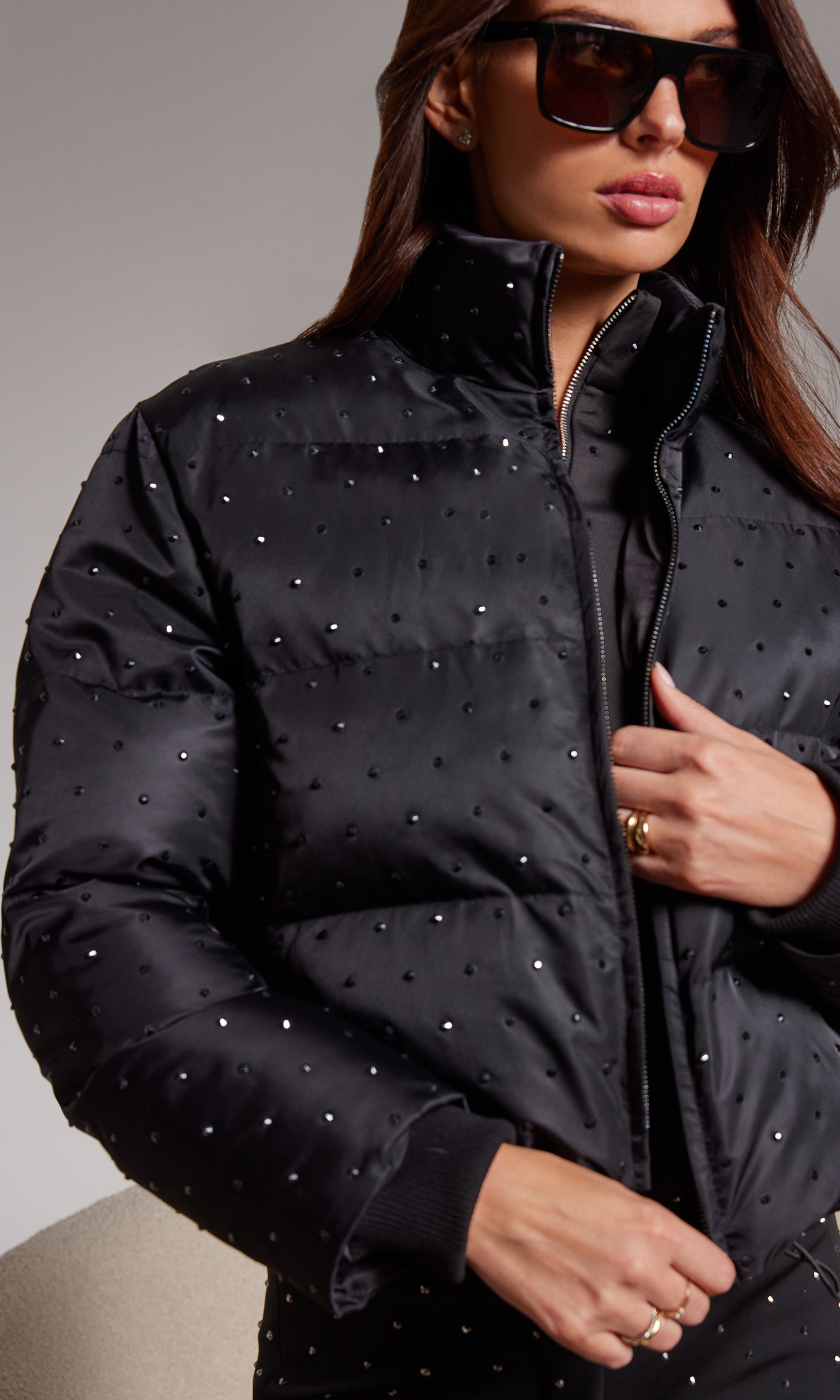 Woman wearing a black quilted jacket with silver studs and sunglasses.