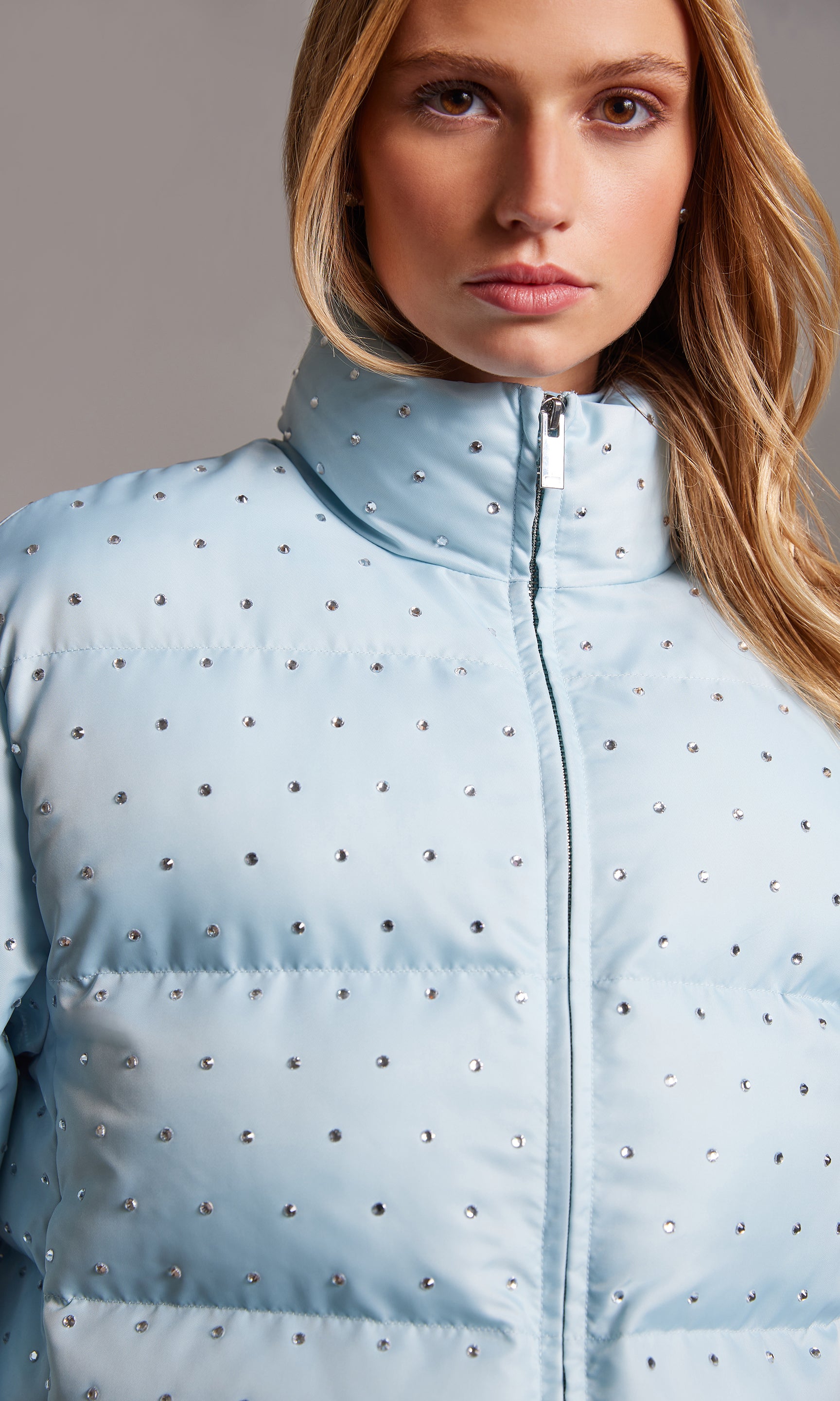 Light blue puffer jacket with decorative studs worn by a model against a neutral background