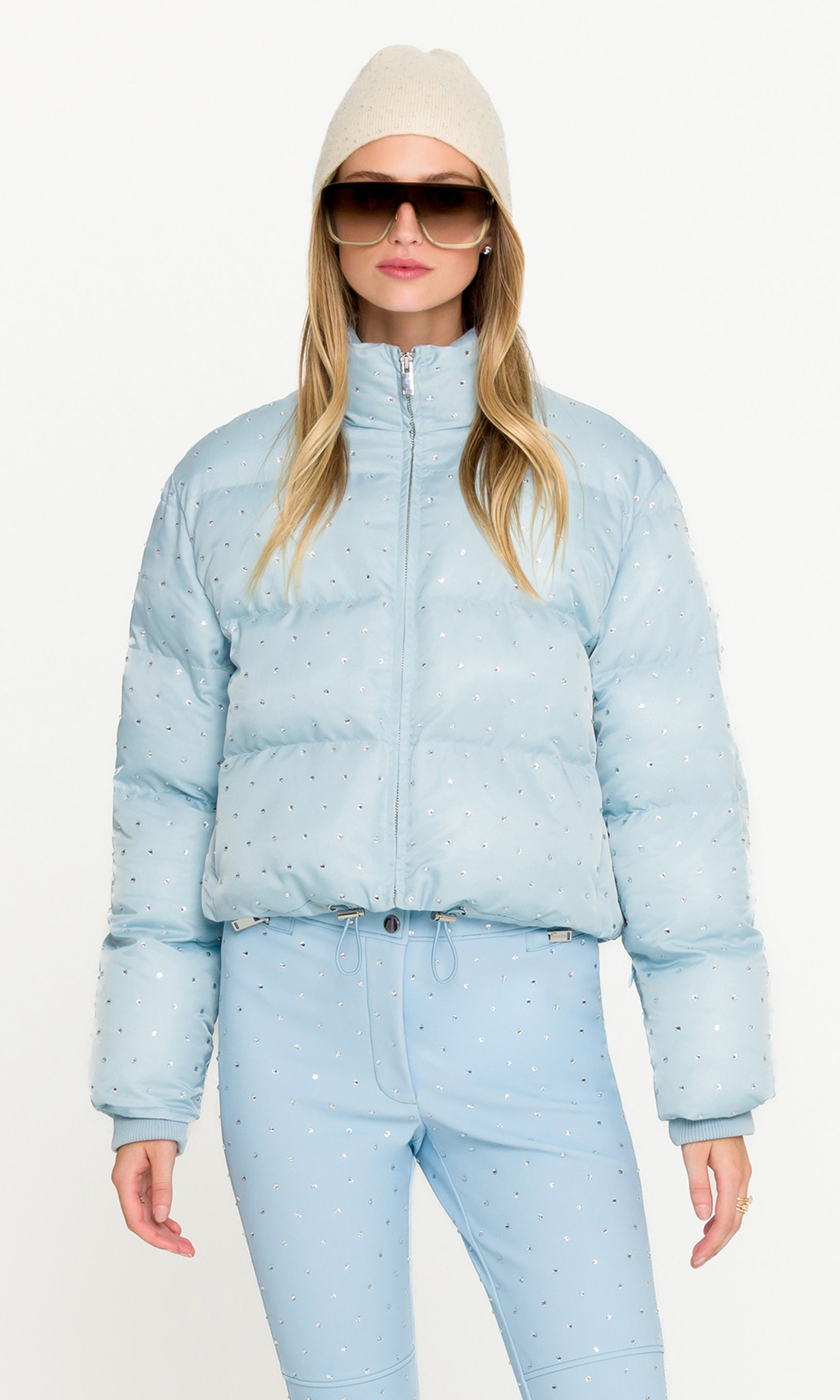 Woman wearing a light blue puffer jacket and pants with a white background