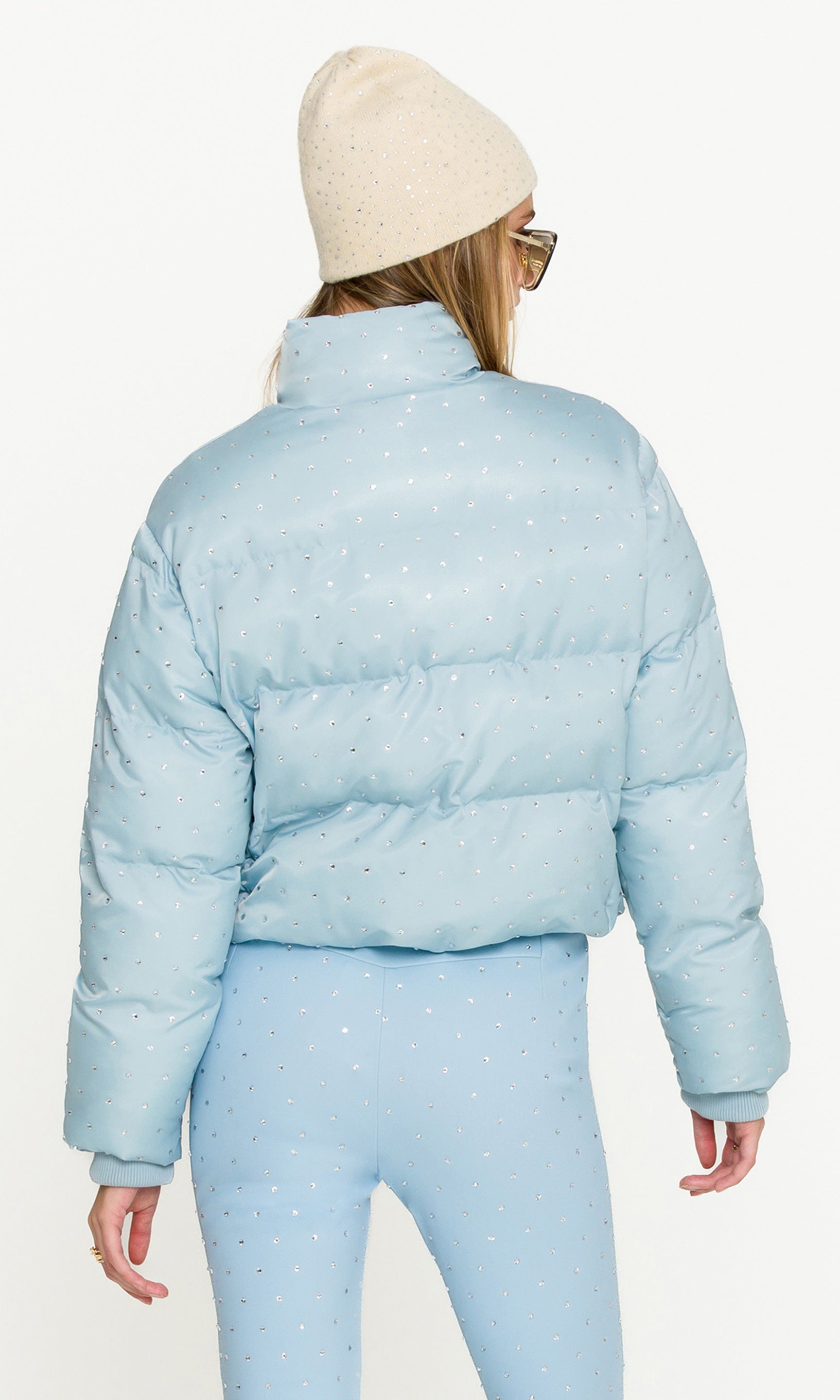 Person wearing a light blue puffer jacket and pants with a white background
