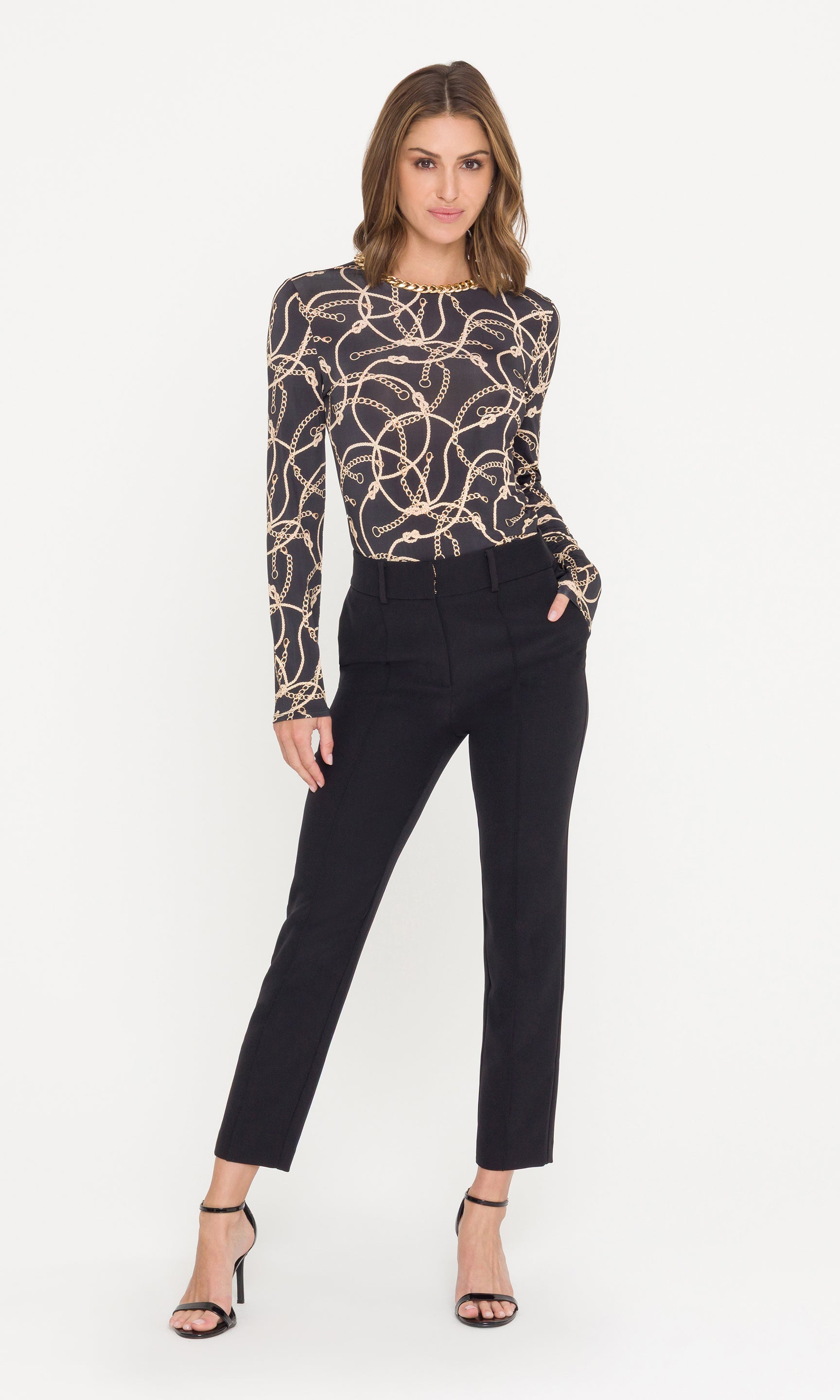 Woman wearing a patterned long-sleeve top and black pants on a white background