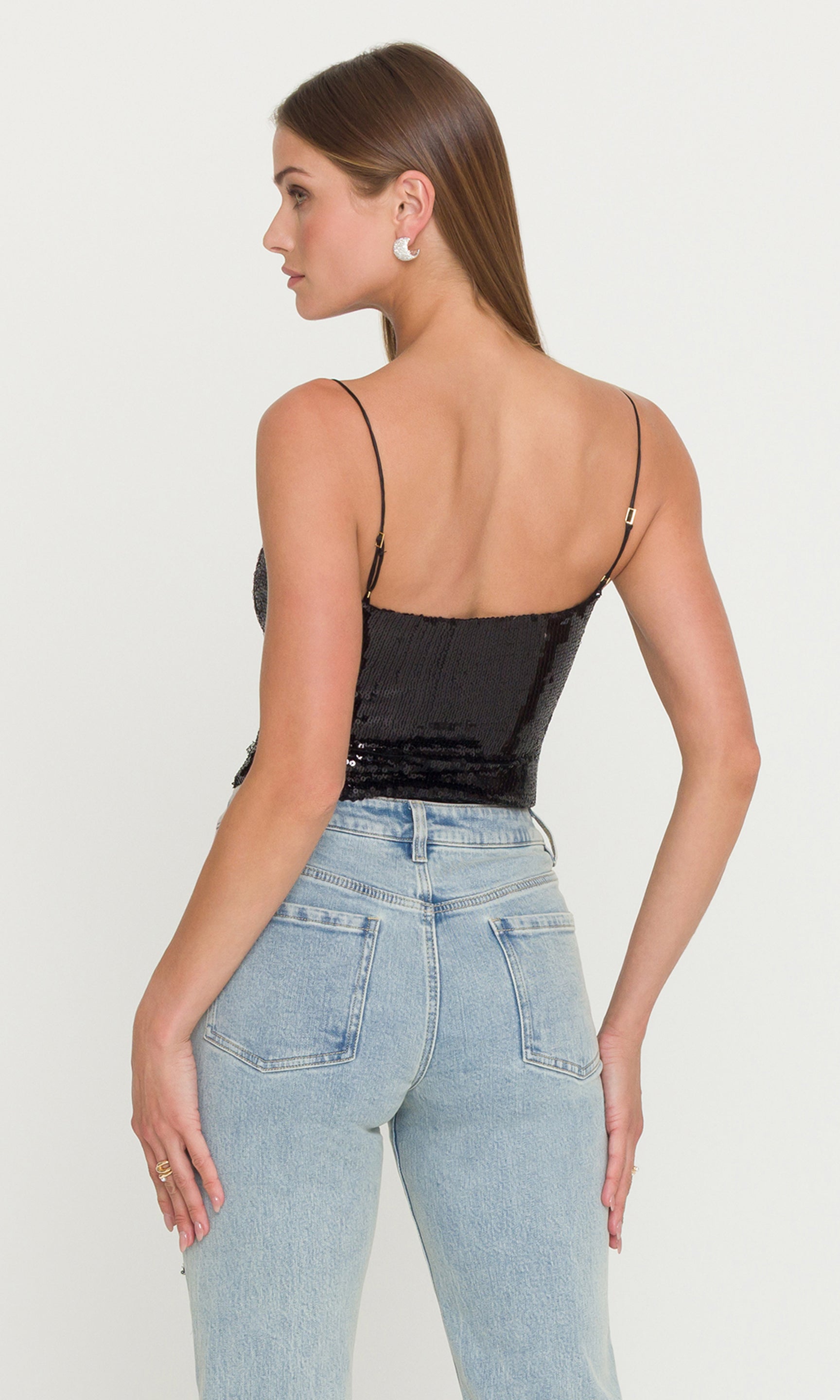 Back view of model wearing a black sequin cami and light blue jeans on a white background