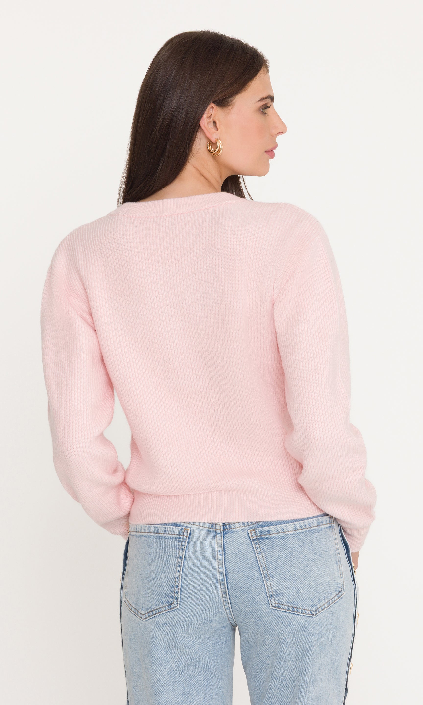 Woman wearing a light pink sweater and light blue jeans against a white background