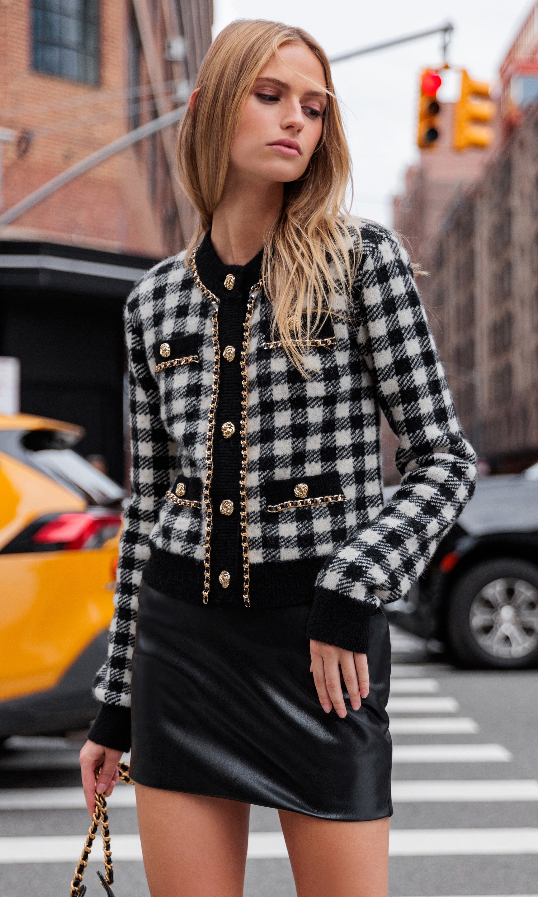 Woman in a black and white checkered cardigan with gold buttons on a city street.