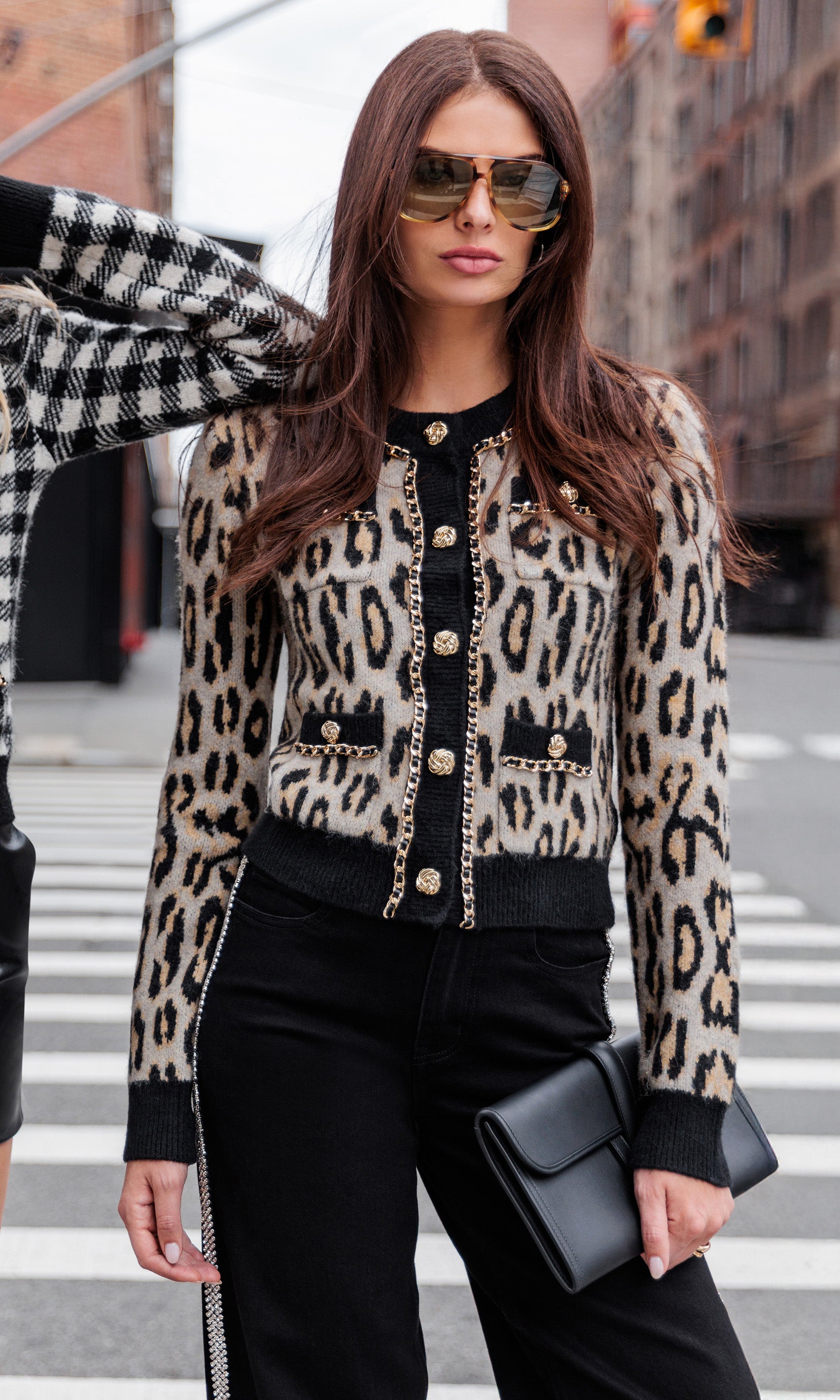 Woman wearing a leopard print cardigan with a cityscape design, standing on a crosswalk.
