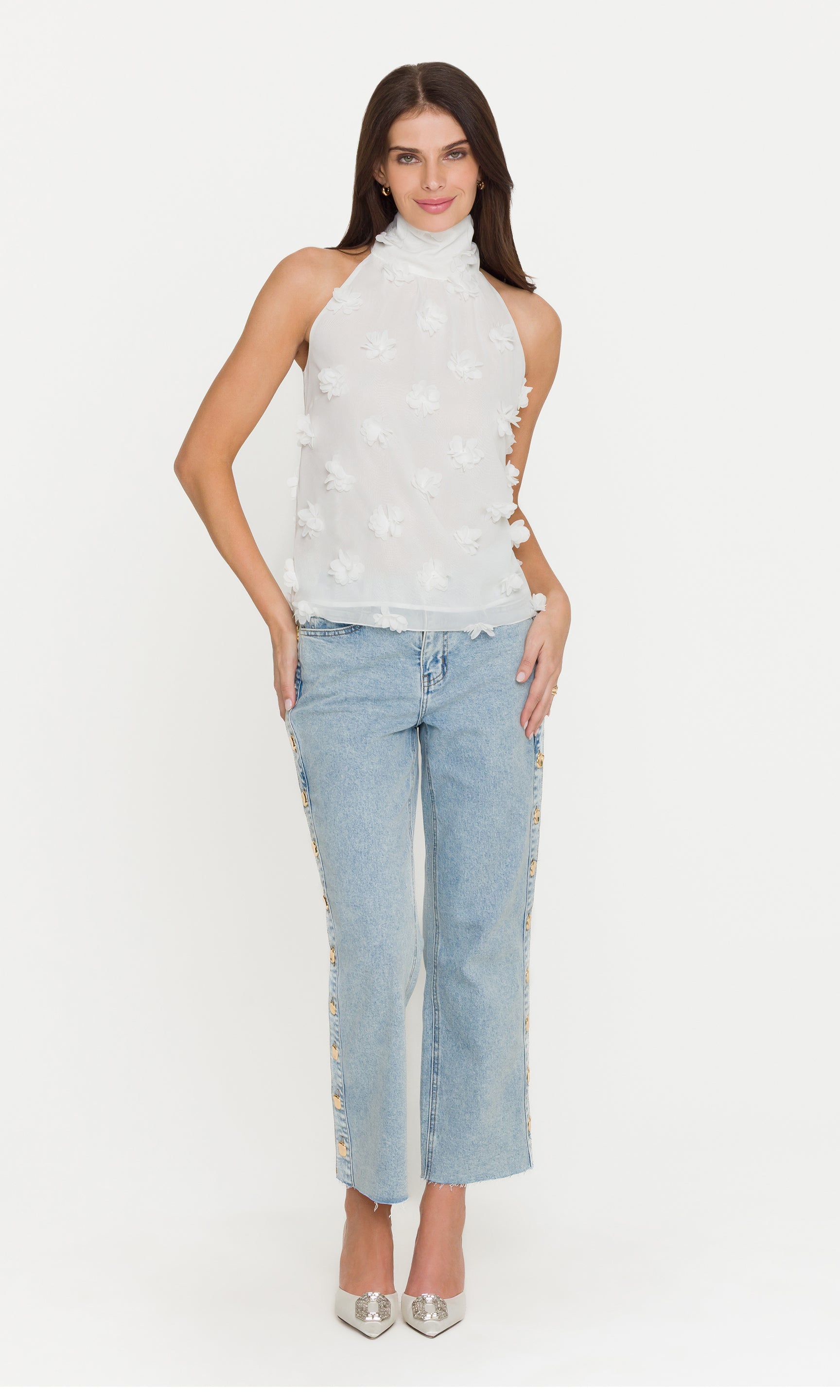 Woman wearing a white sleeveless top with flower details and light blue jeans on a white background