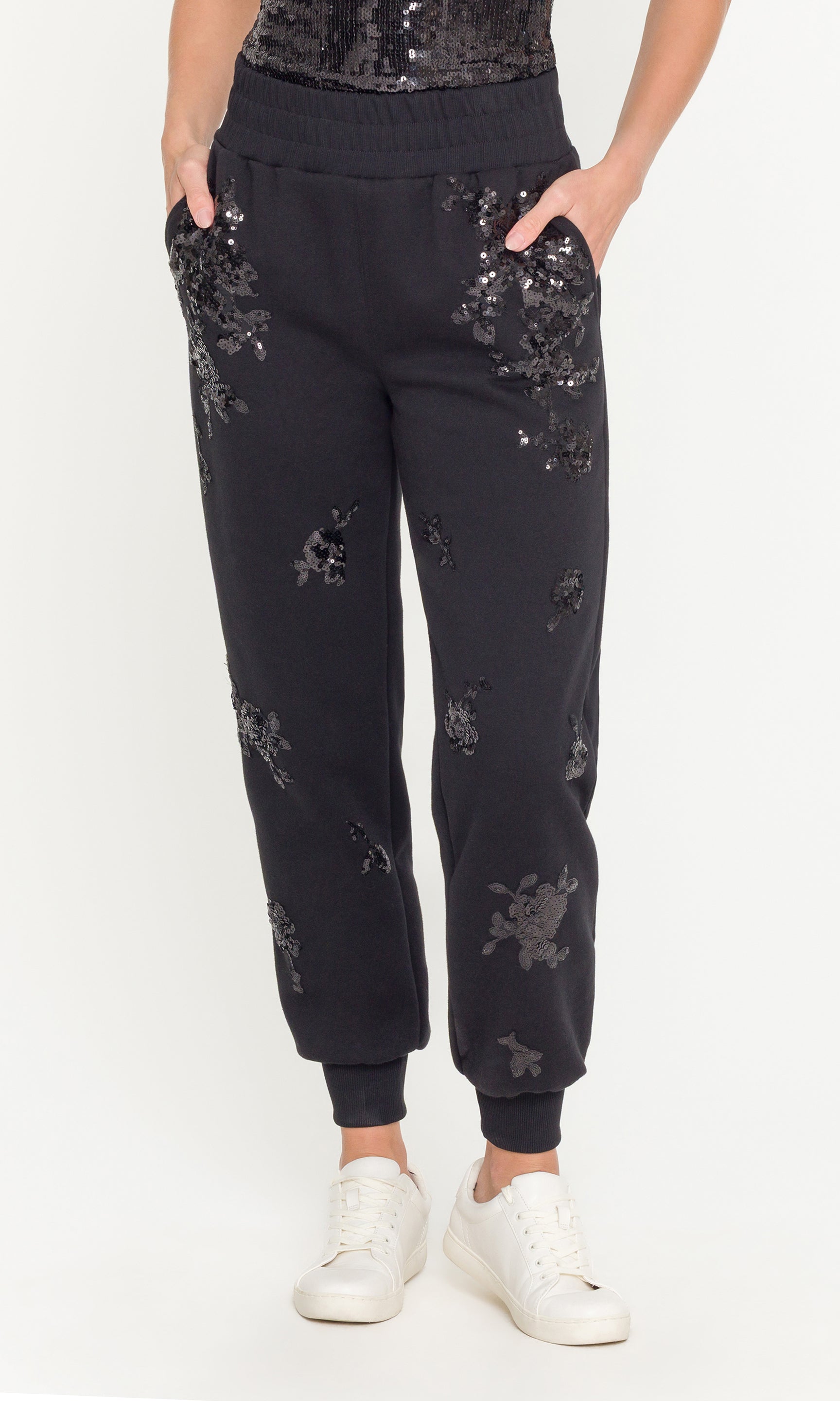 Black jogger pants with sequin embellishments worn by a person on a white background