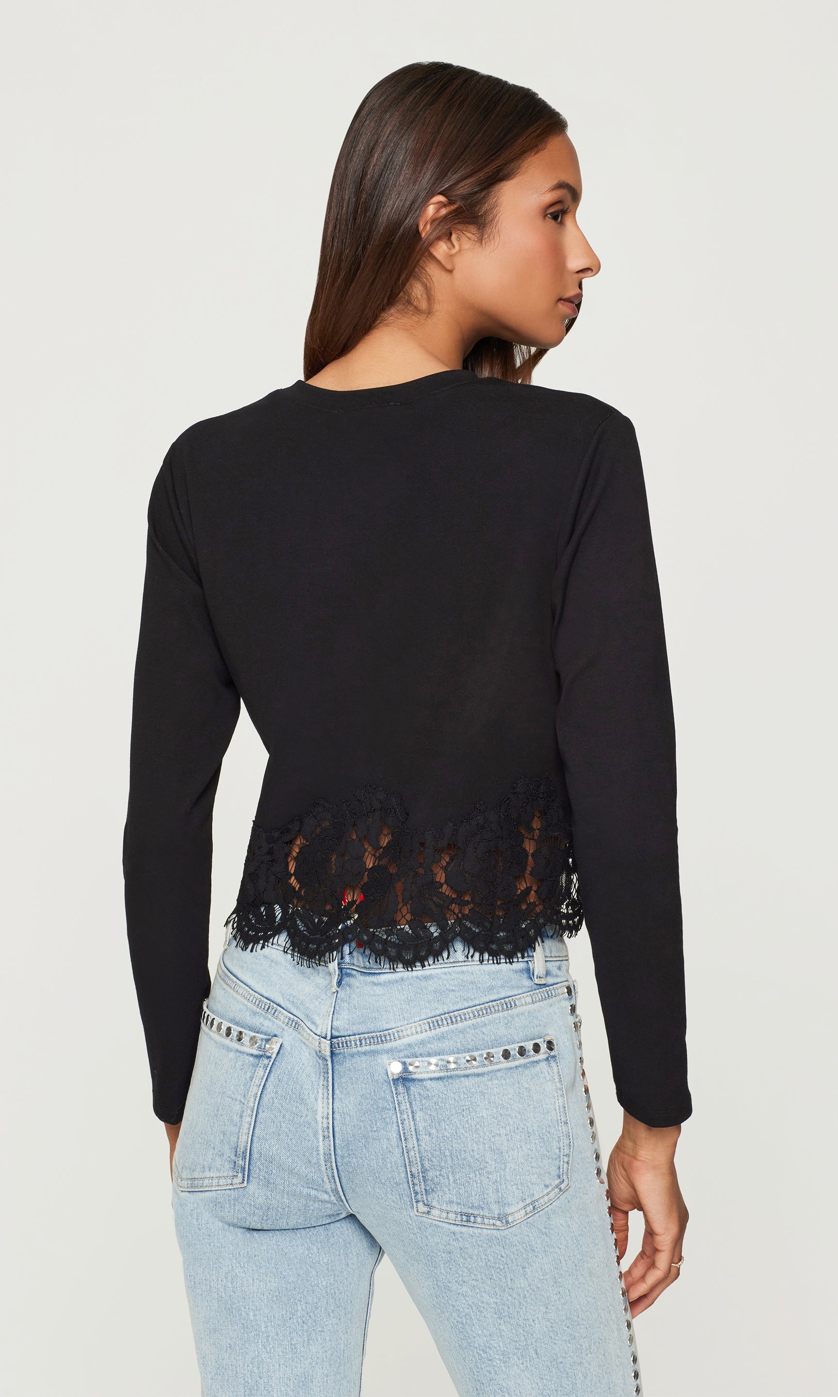 Back view of person wearing a black long-sleeve top with lace detailing and light blue jeans on a white background