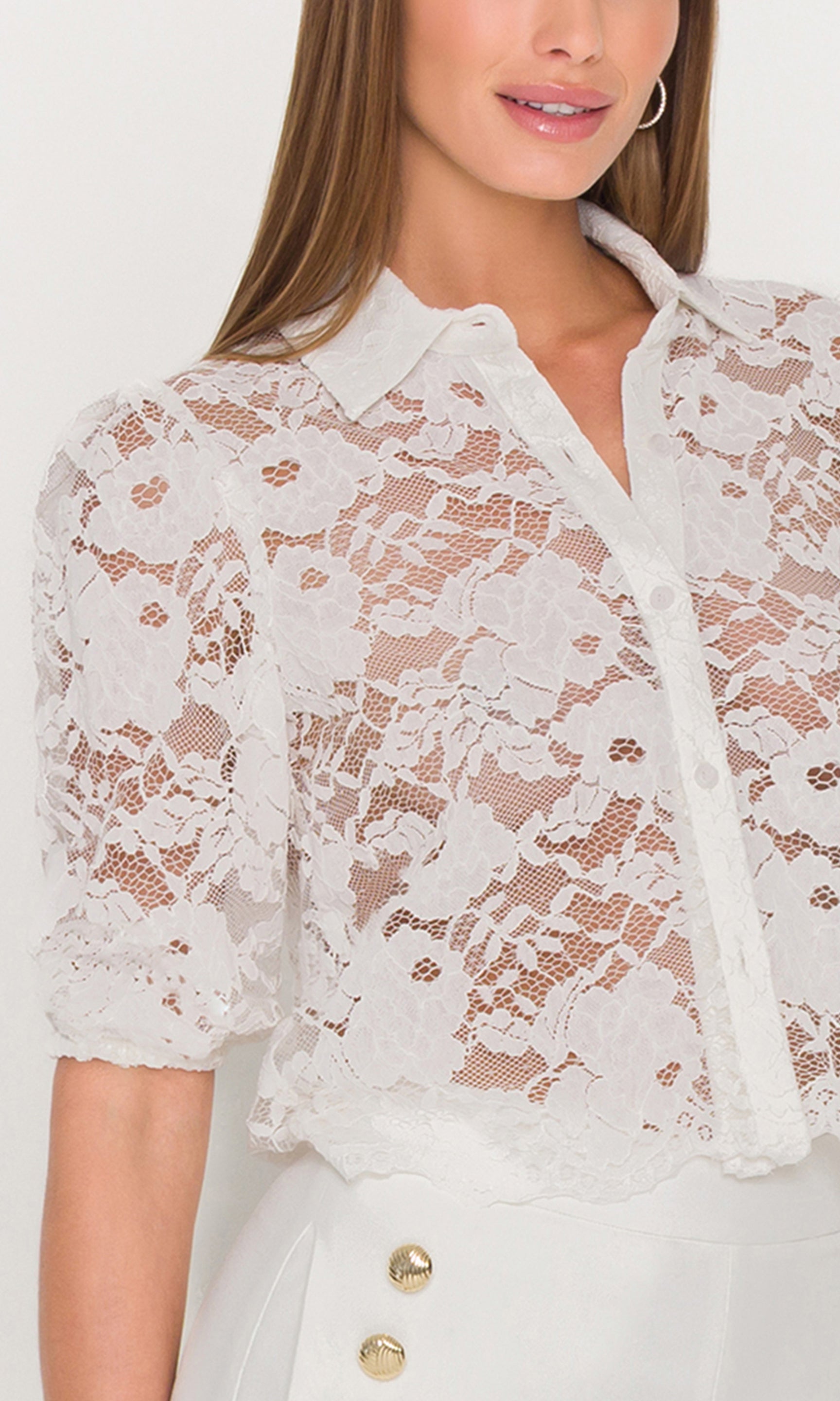 Close-up of white lace blouse with floral details on a plain background