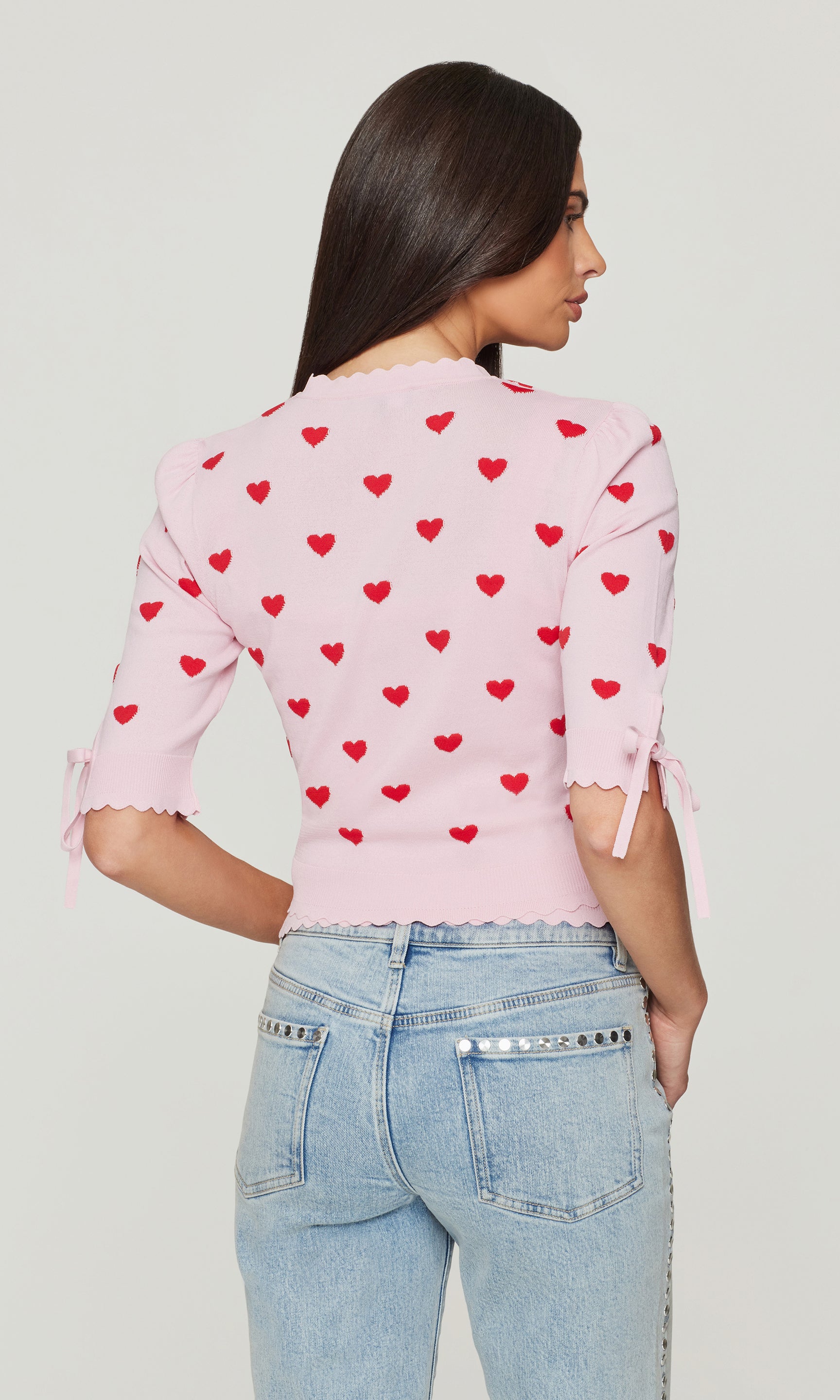 Back view of woman wearing a pink cardigan with red hearts on a white background
