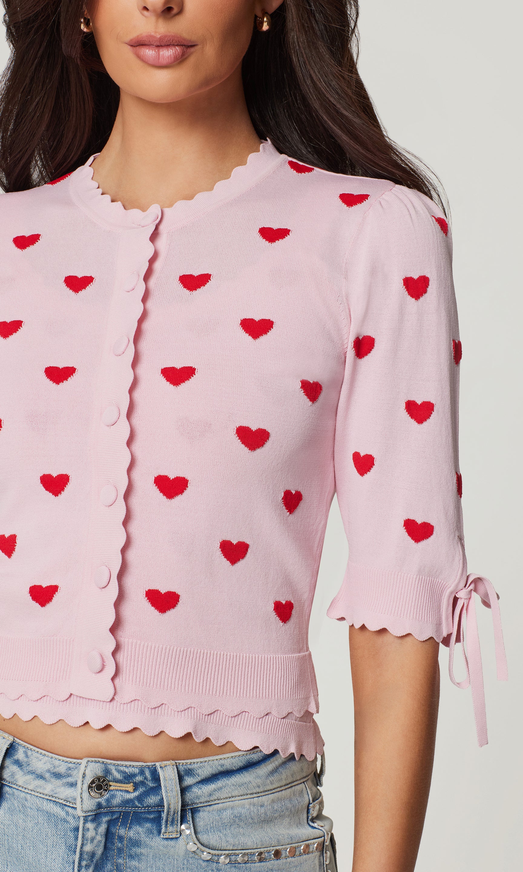 Close-up of pink cardigan with red heart patterns worn by a person on a plain background