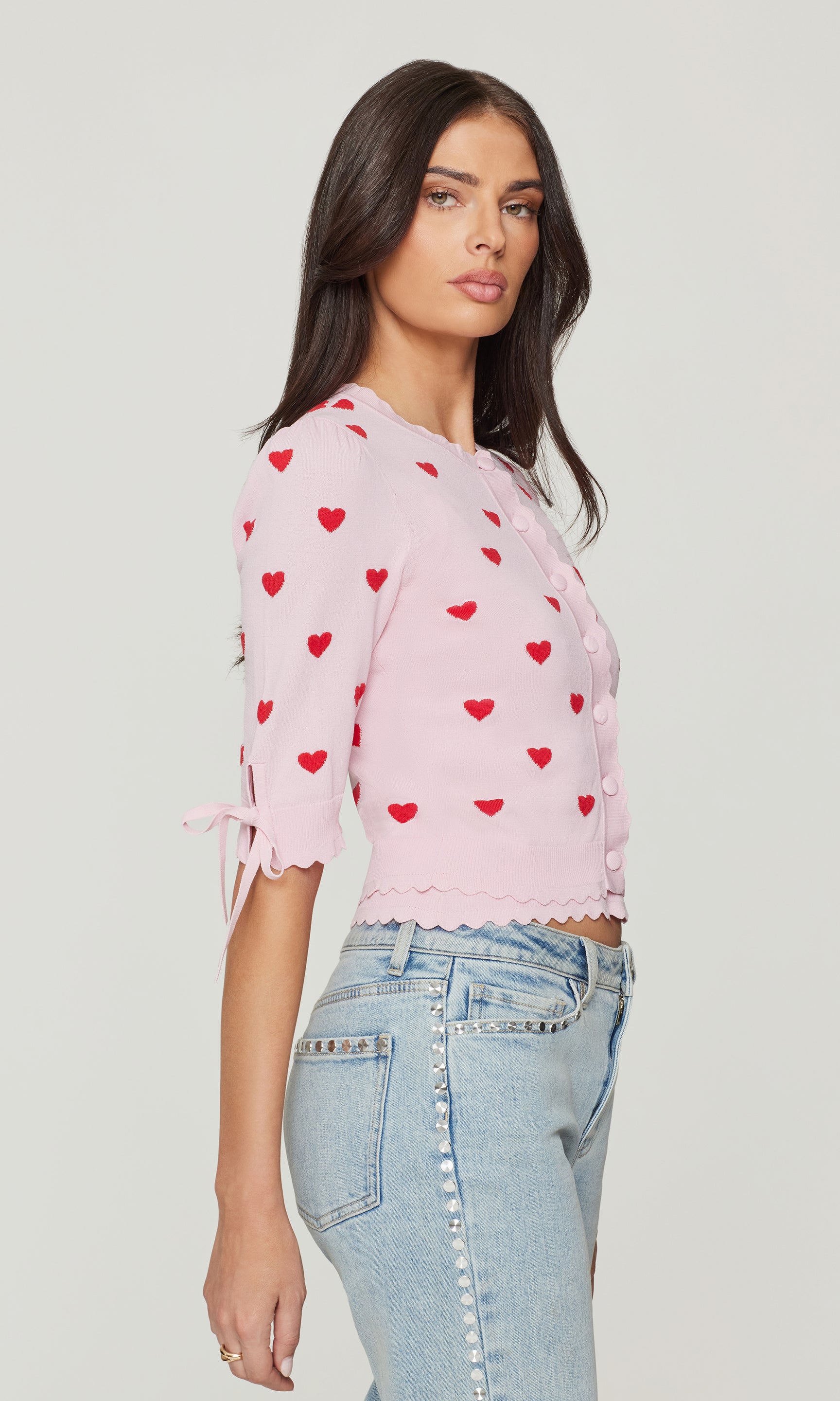 Side view of woman wearing a pink cardigan with red hearts on a white background