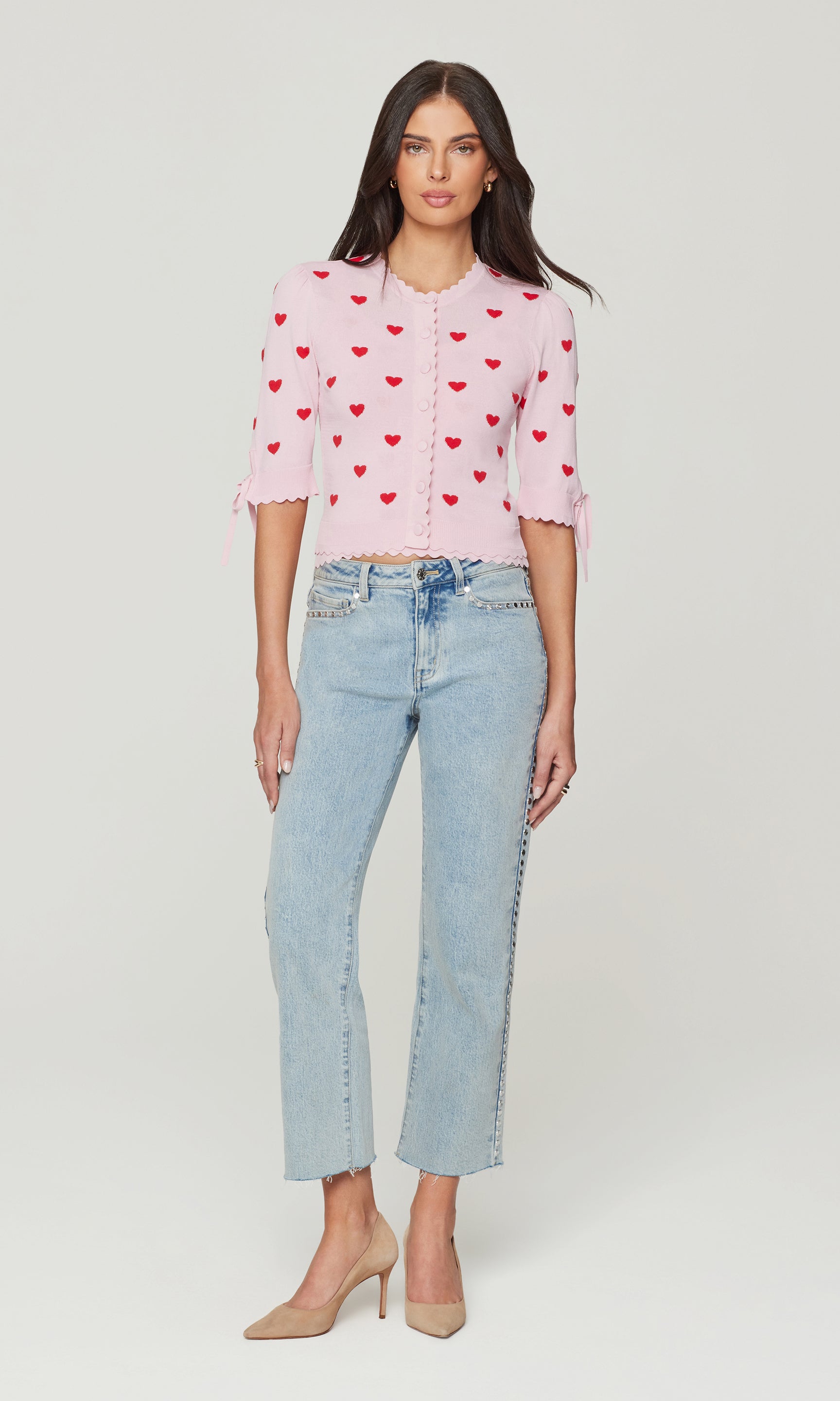 Woman wearing a pink blouse with red heart patterns and light blue jeans on a white background