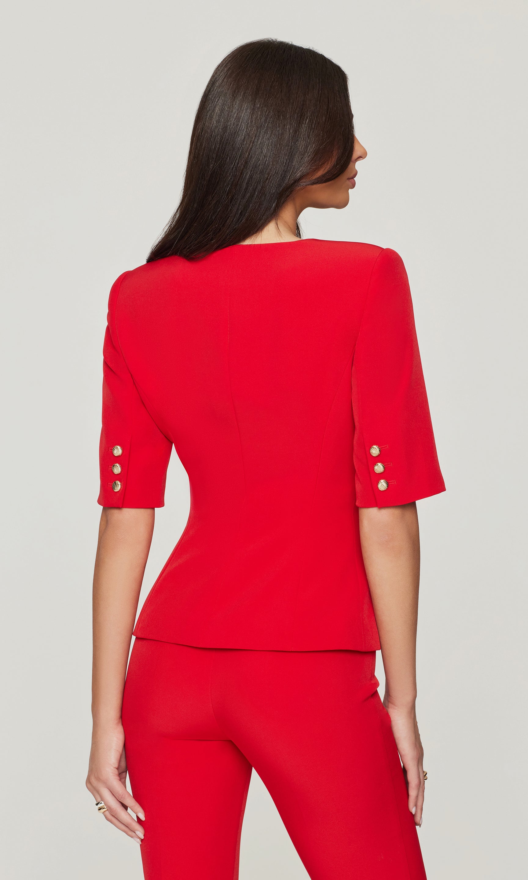 Back view of woman wearing a red outfit with button details on a light gray background
