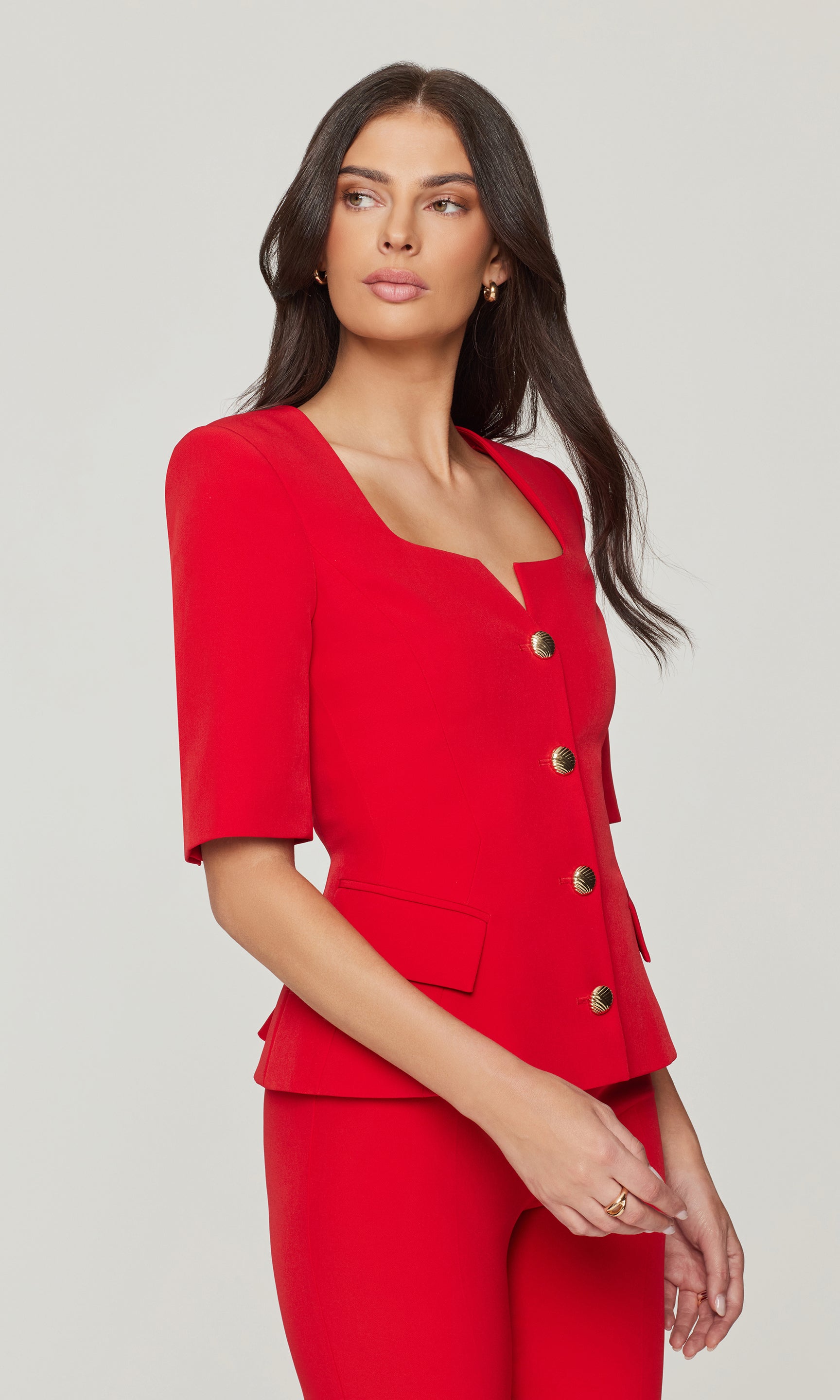 Side view of woman wearing a red suit with black buttons on a gray background