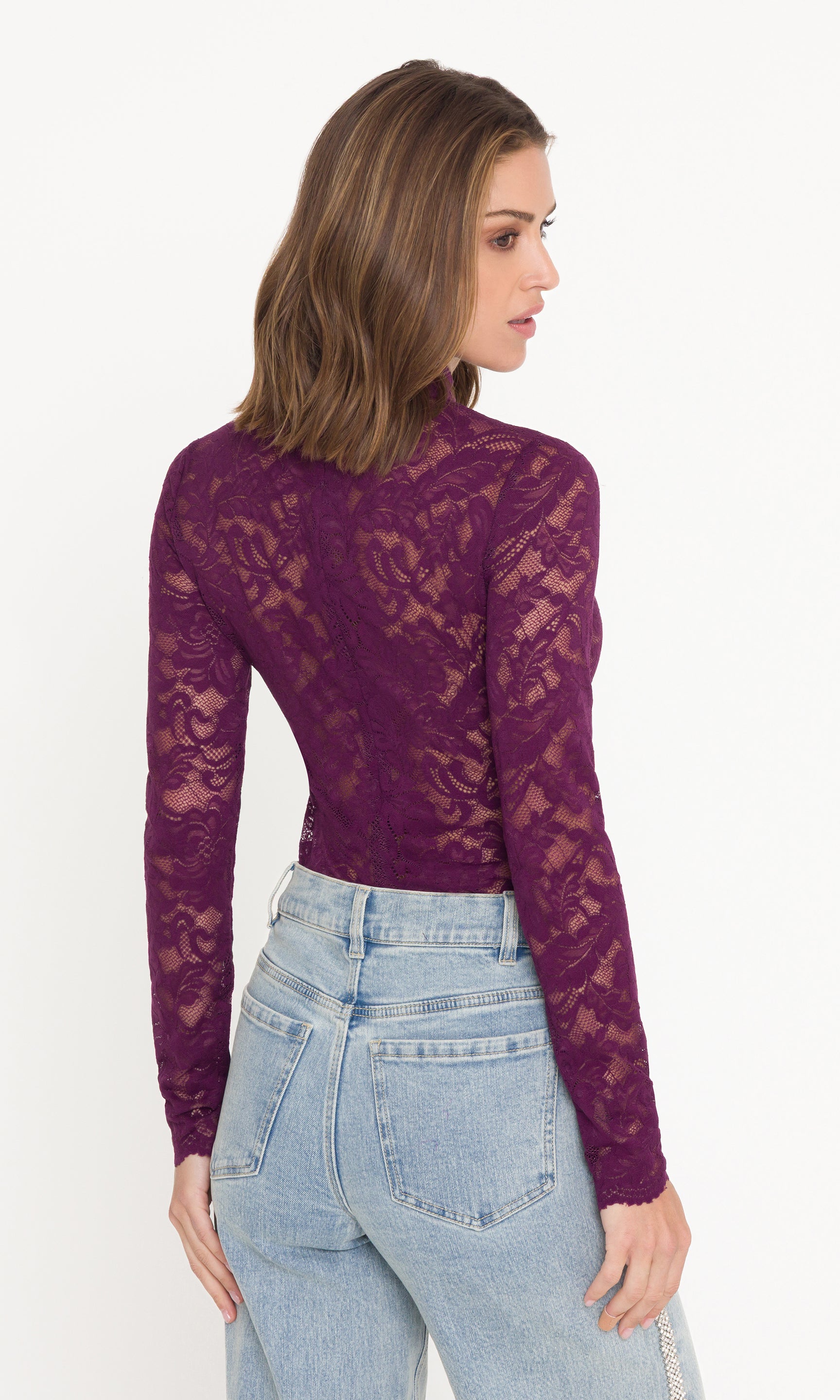 Back view of model wearing a purple lace long-sleeve top and light blue jeans on a white background