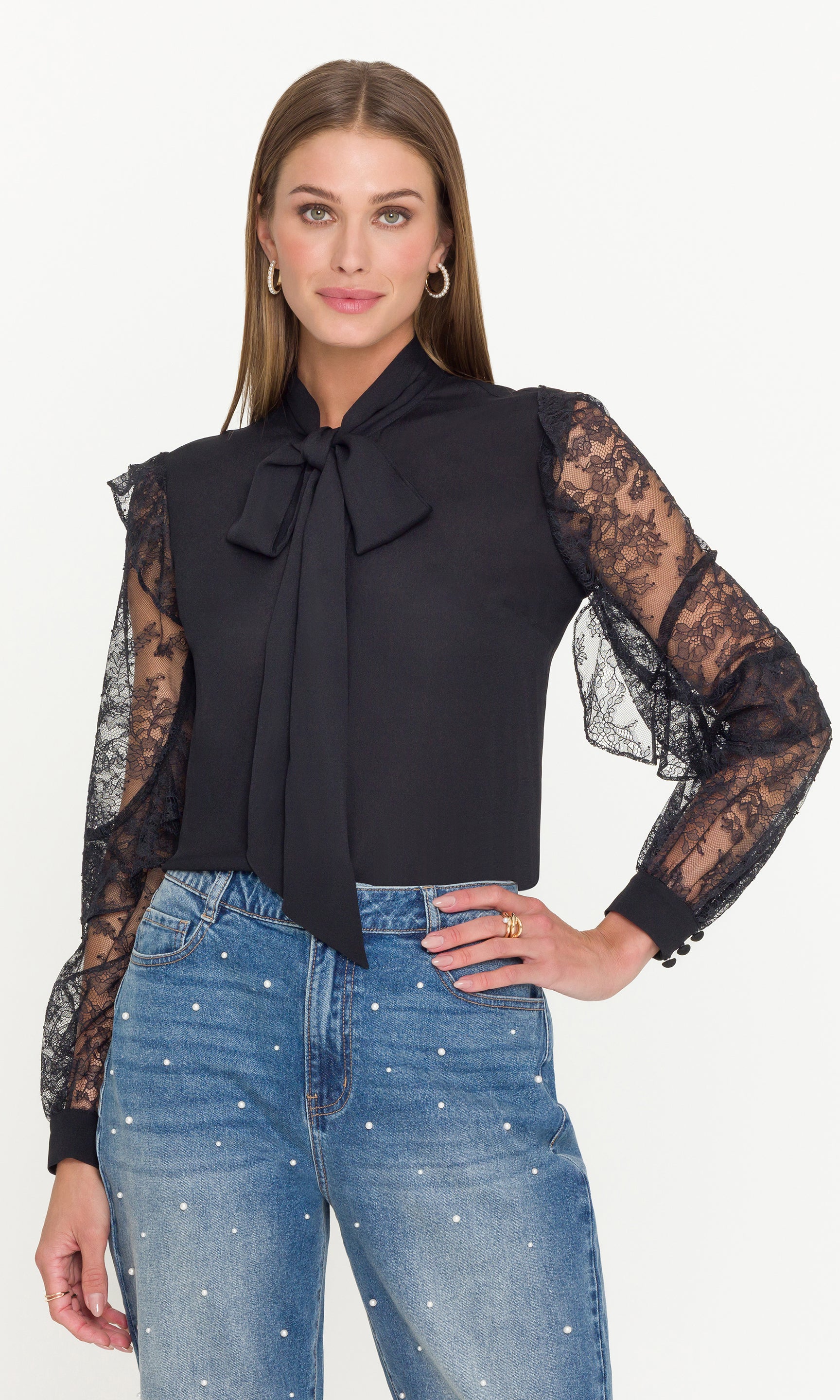 Woman wearing a black blouse with lace sleeves and blue jeans on a white background