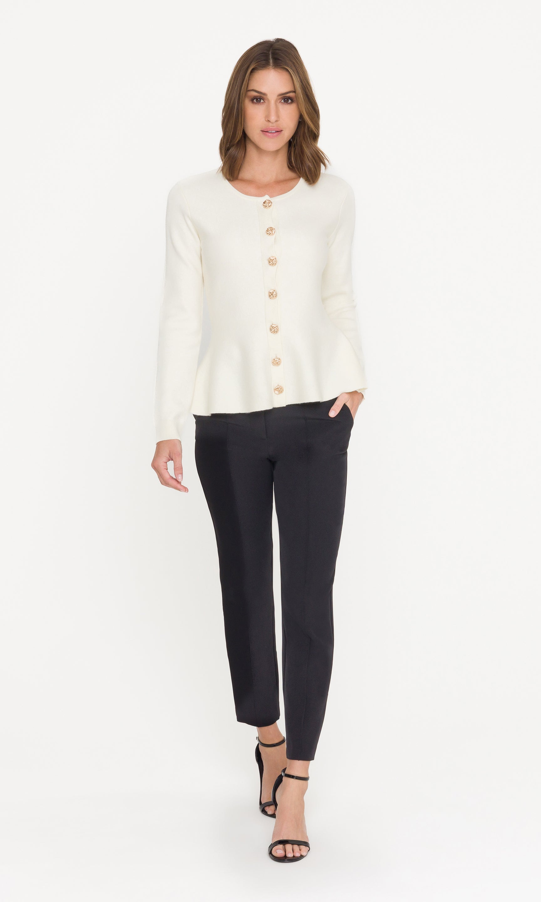 Woman wearing a white peplum cardigan with buttons and black pants on a white background