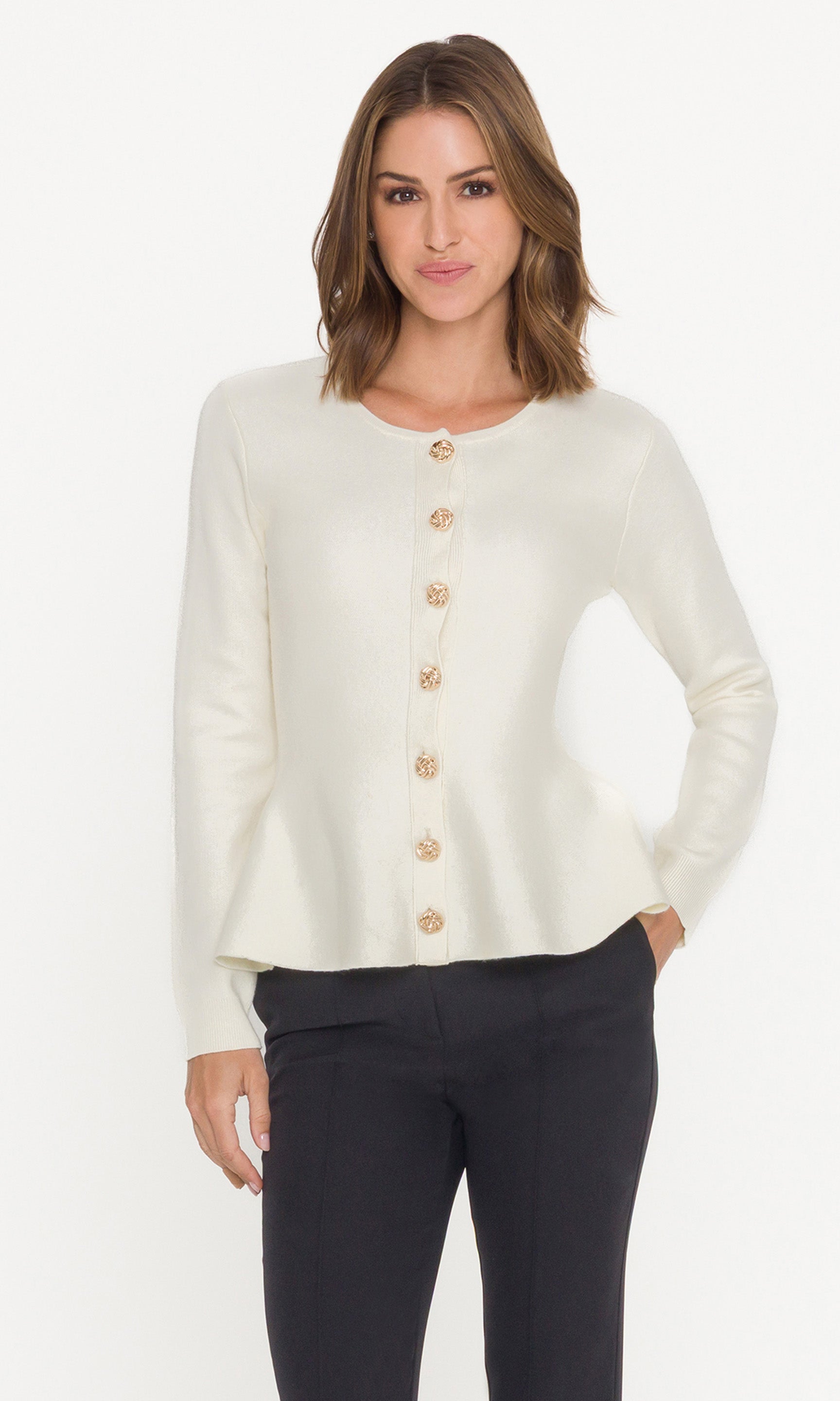 Woman wearing a cream cardigan with gold buttons and black pants on a white background