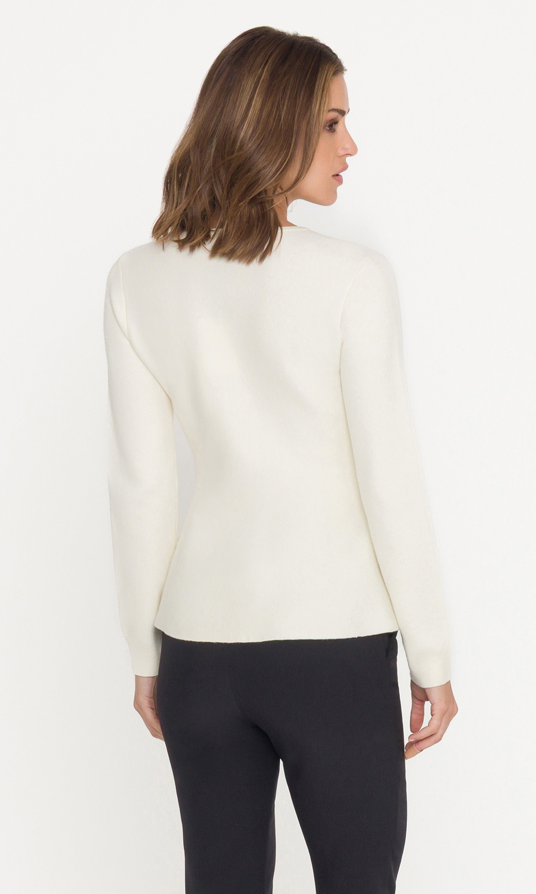 Back view of woman wearing a cream cardigan with gold buttons and black pants on a white background