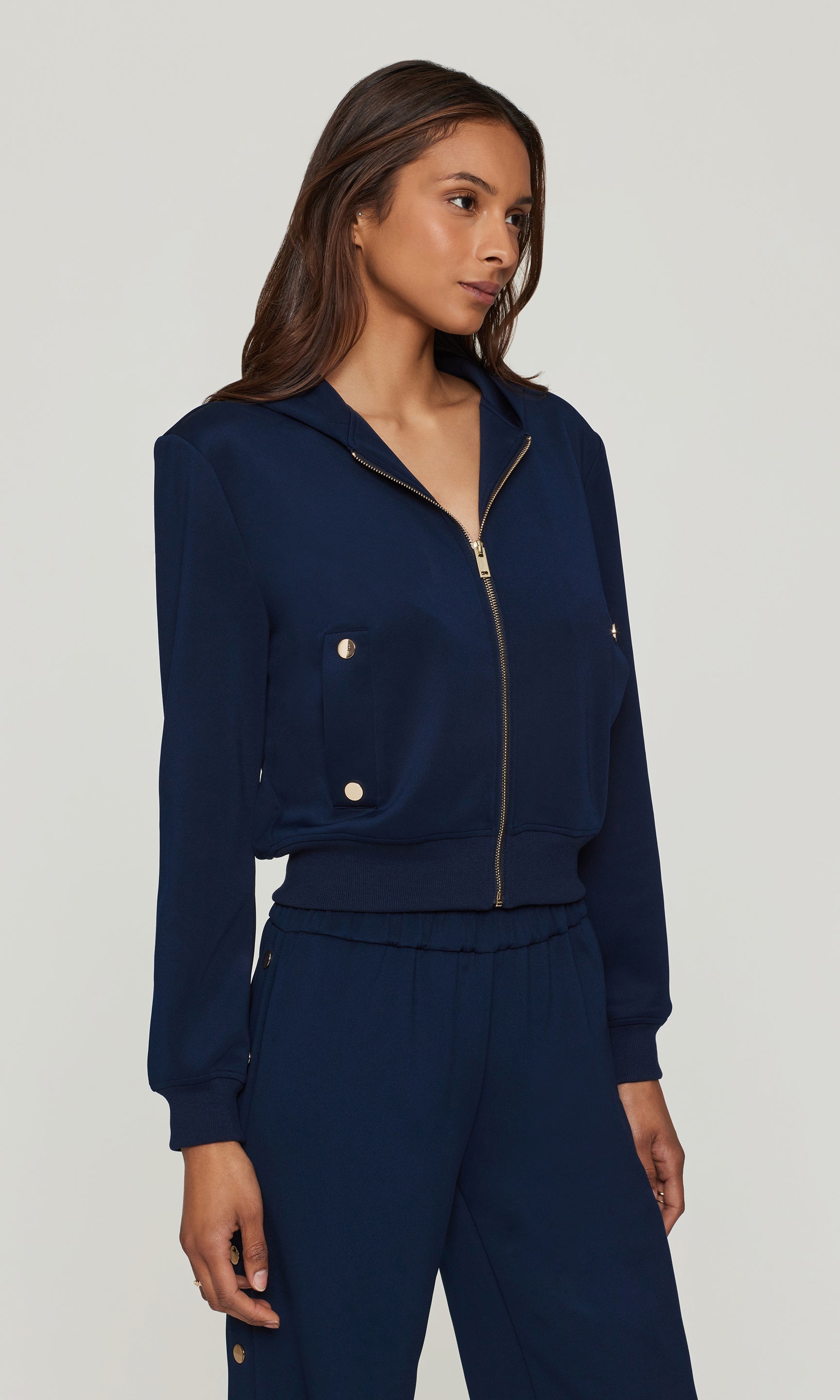 Side view of woman wearing a navy blue tracksuit on a plain background