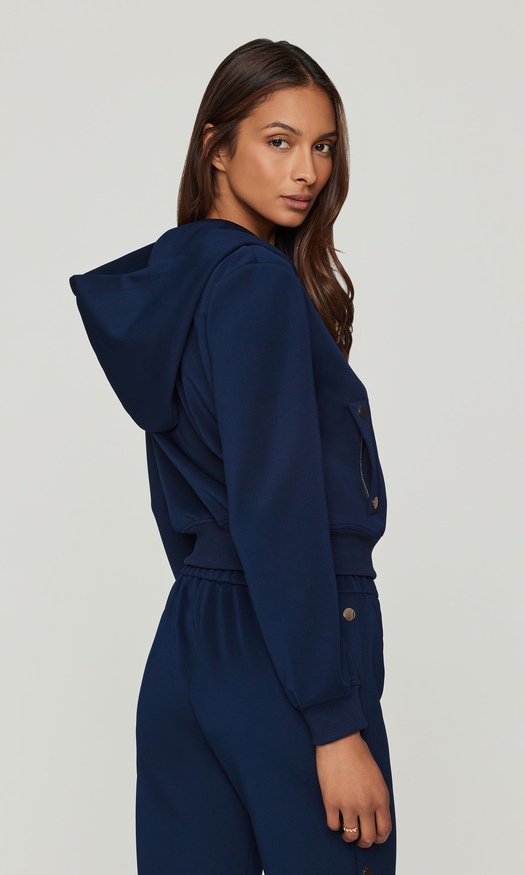 Back view of foman wearing a navy blue hoodie and pants on a light gray background