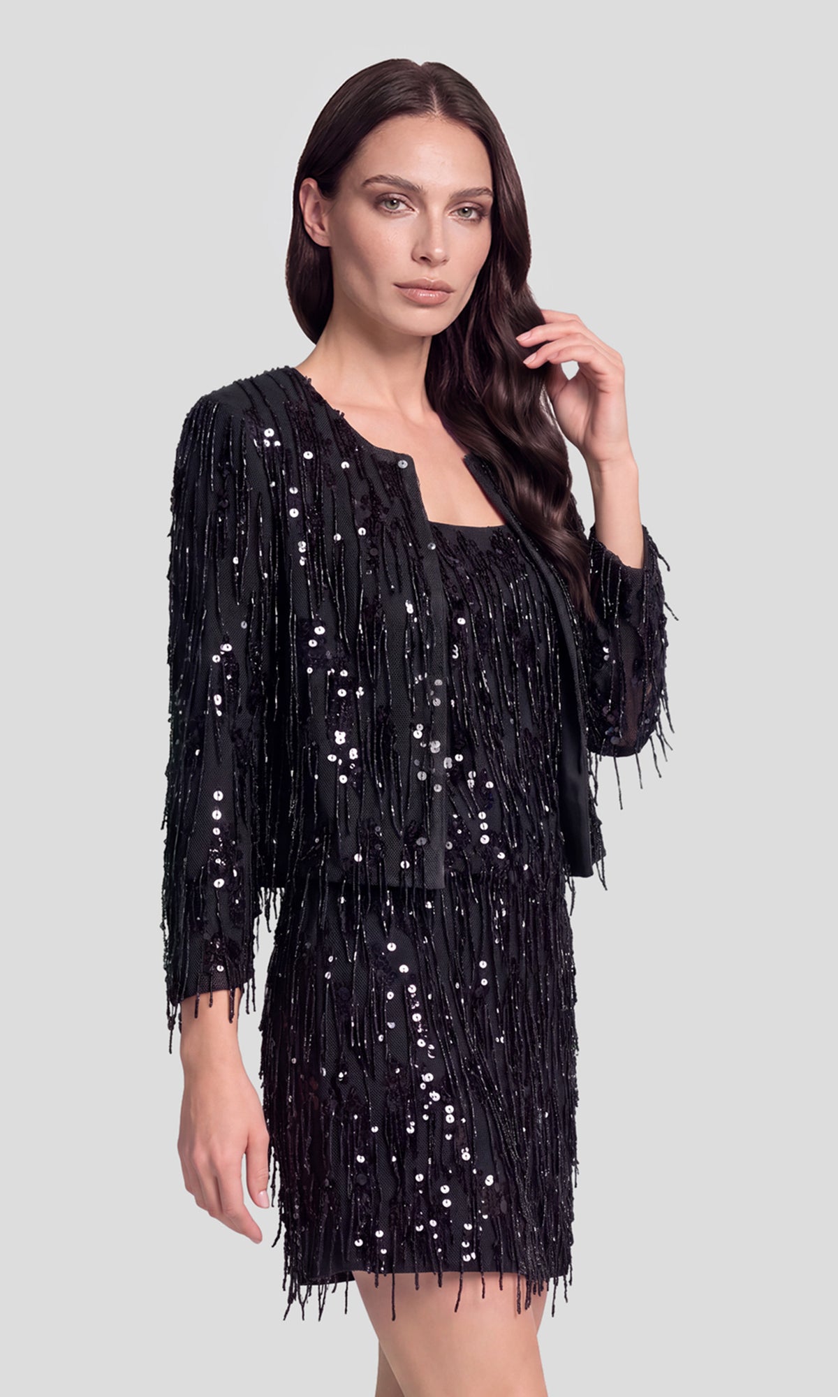 Side view of model wearing a black fringe sequins jacket over a matching fringe sequins cami and skirt.