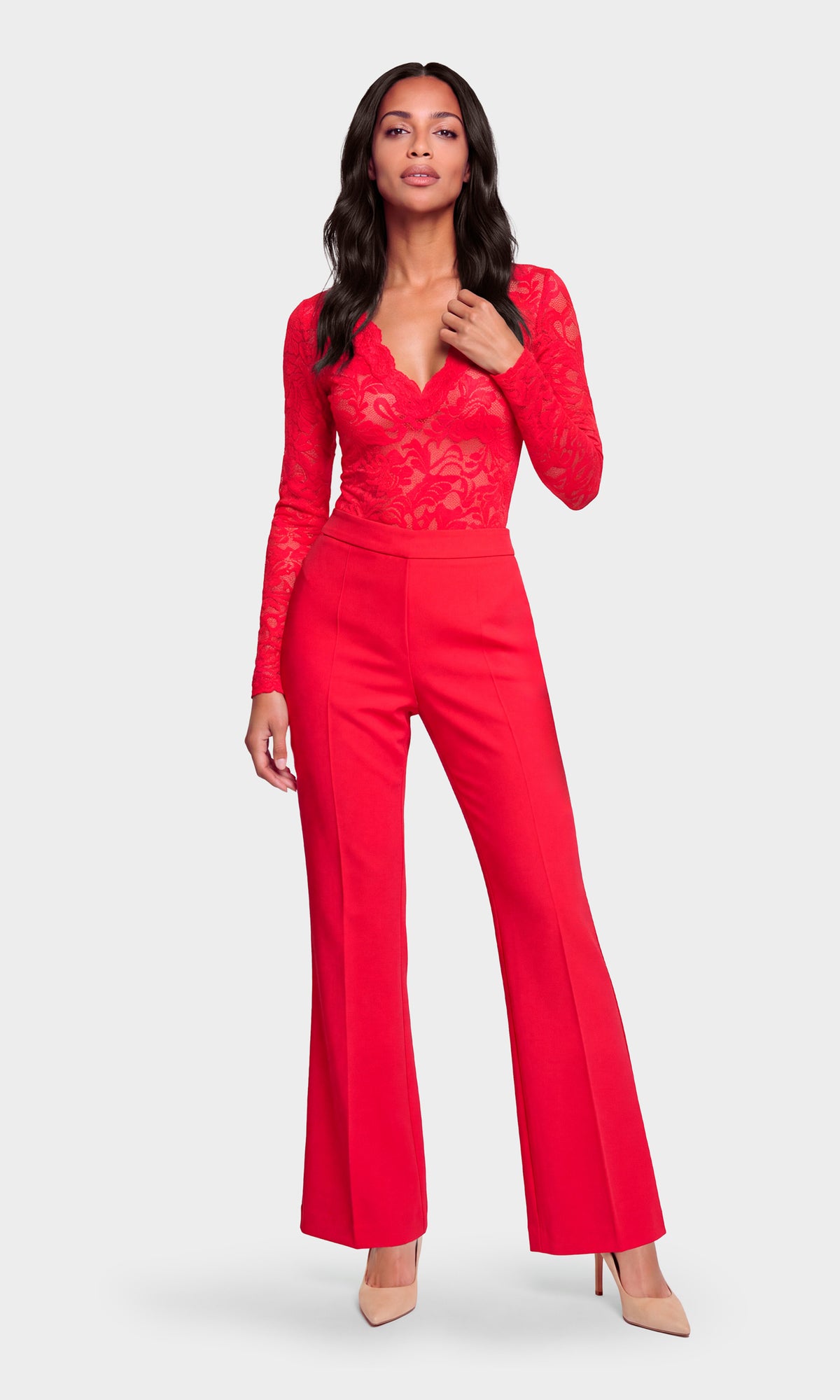 Model wearing a bright red long-sleeve jumpsuit with a lace bodice and wide-leg trousers, paired with nude heels.