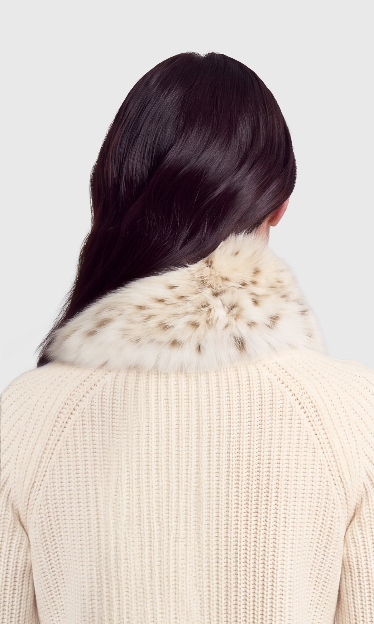 Back view of a person wearing a cream ribbed knit sweater with a fluffy cream and brown fur collar.