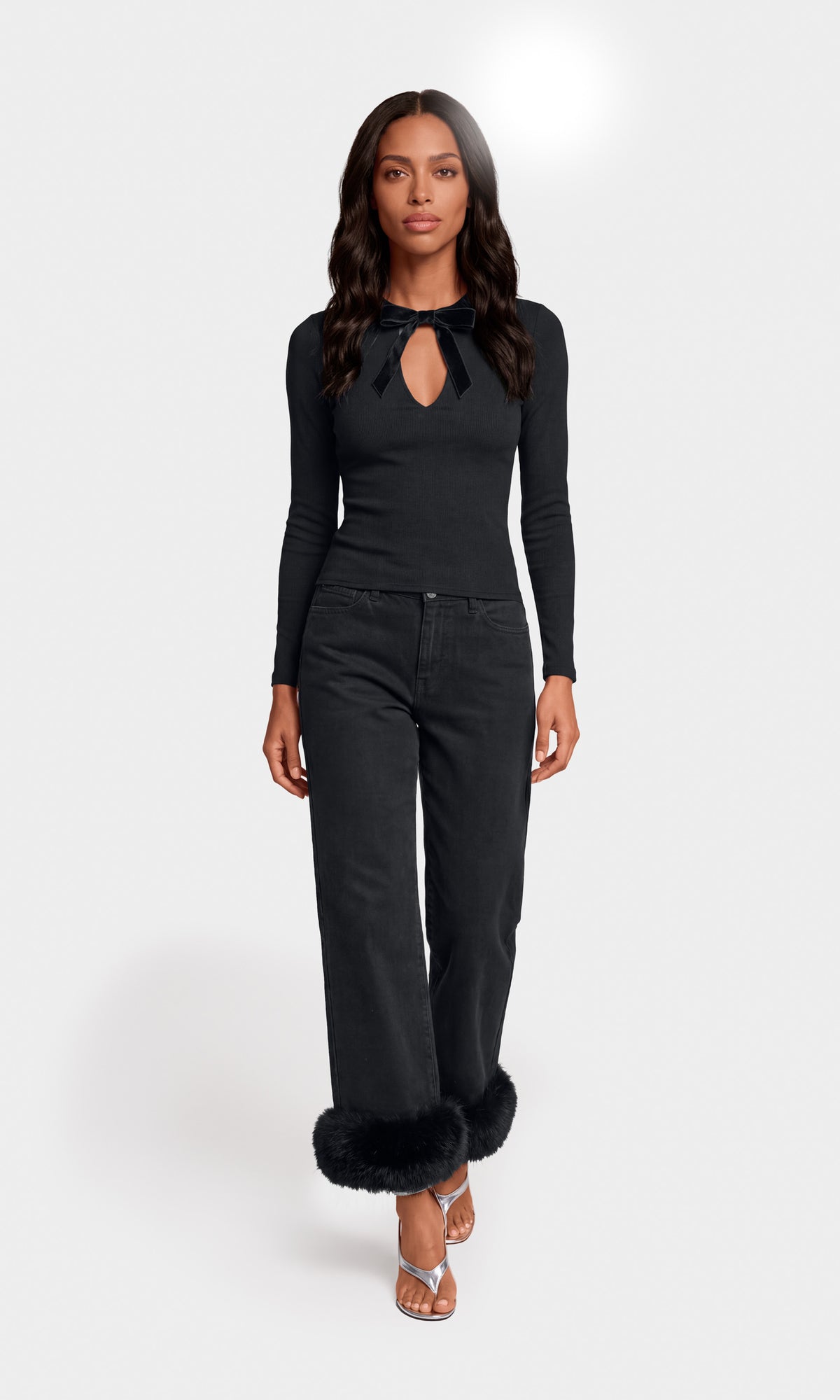 Model wearing a black long-sleeve knit top with a keyhole cutout and tie detail, paired with black wide-leg jeans featuring fluffy black faux-fur trim at the cuffs.