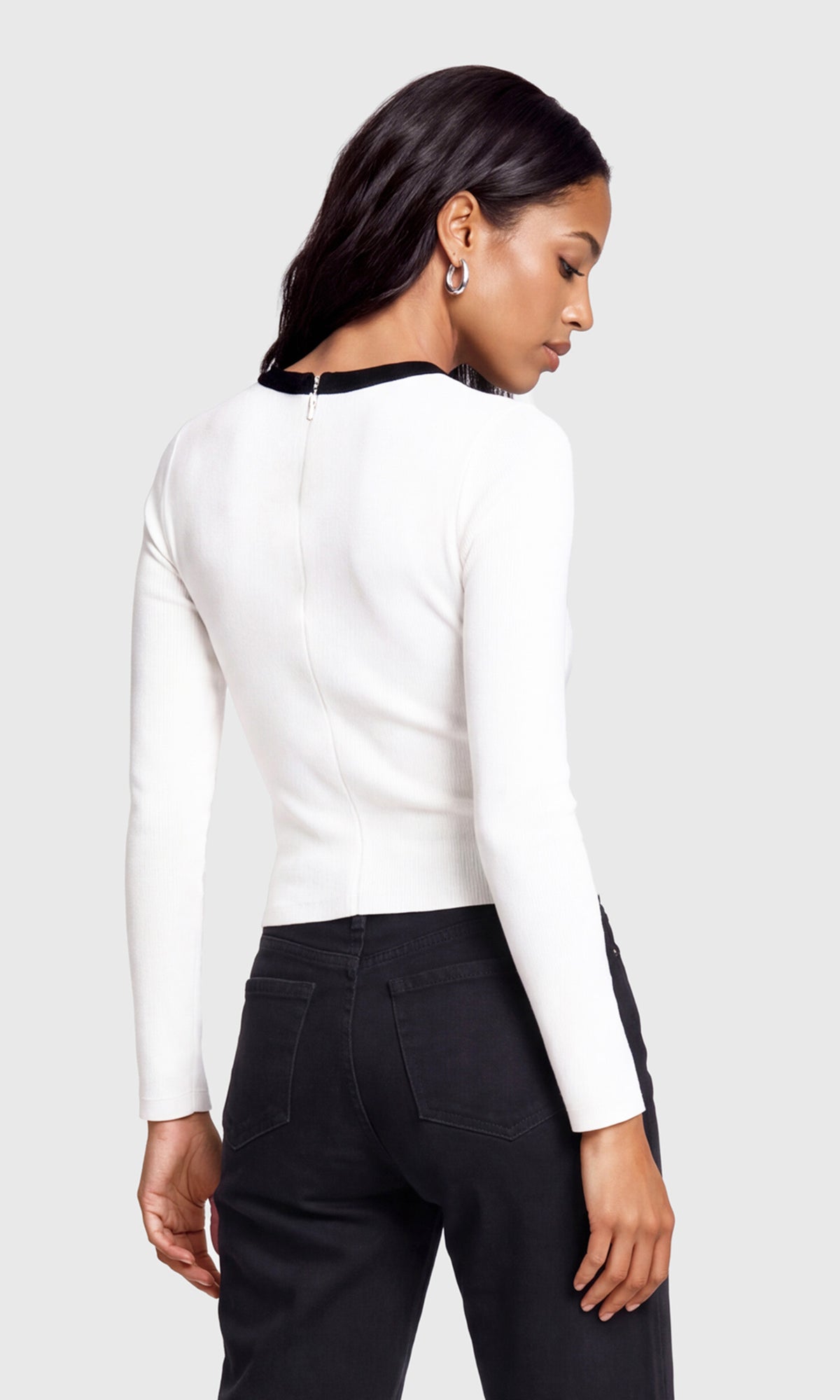 A woman shown from the back wearing a fitted white long-sleeve top with a contrasting black collar trim.