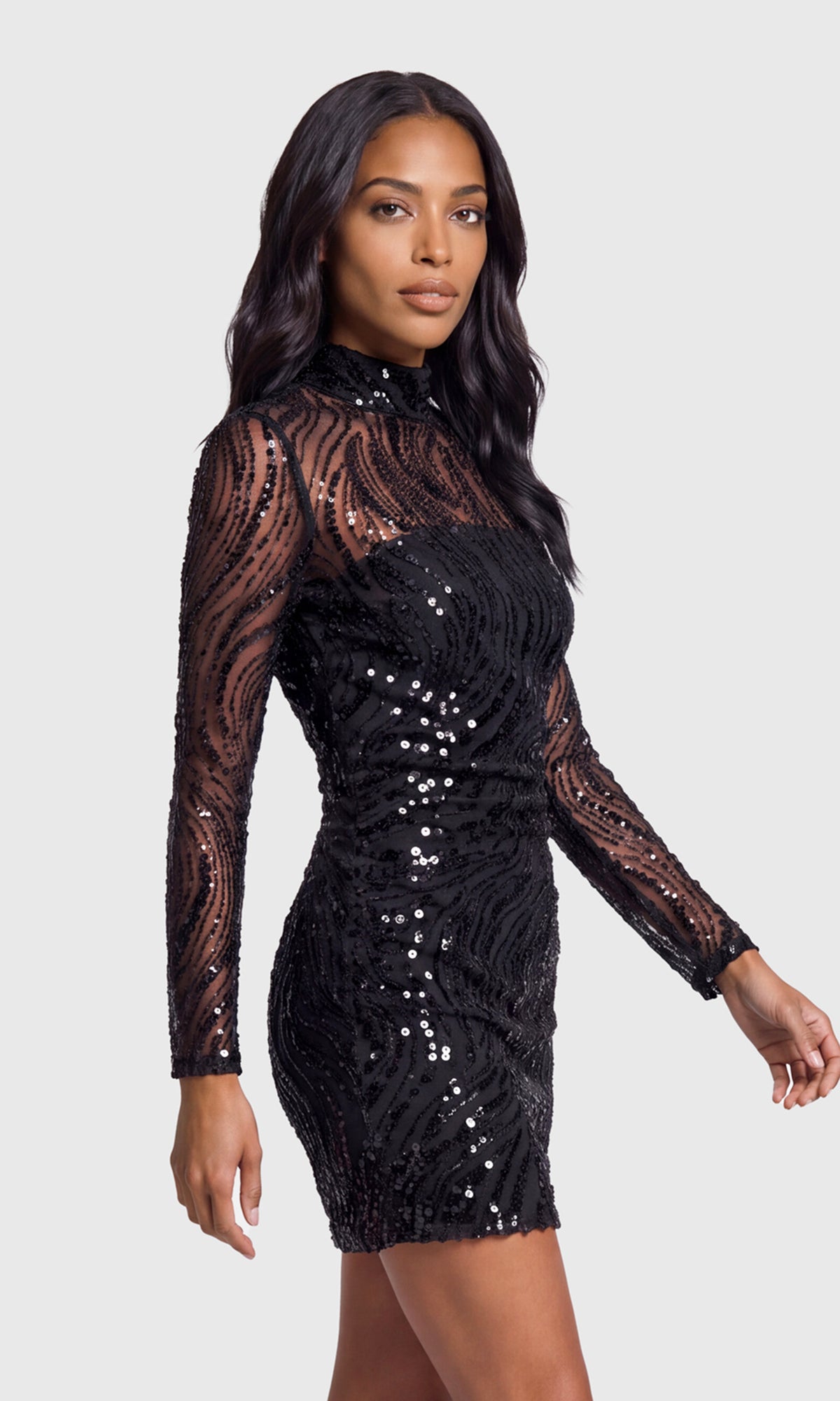 Side view of model wearing a black long-sleeve mini dress with sheer lace sleeves, a high mock neck, and all-over sequined detailing.