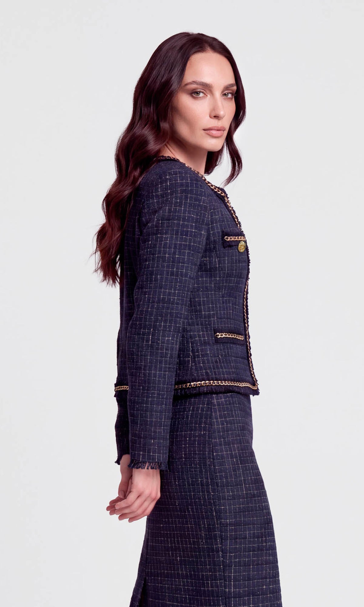 Side view of model wearing a navy tweed jacket with gold accents and a matching skirt.