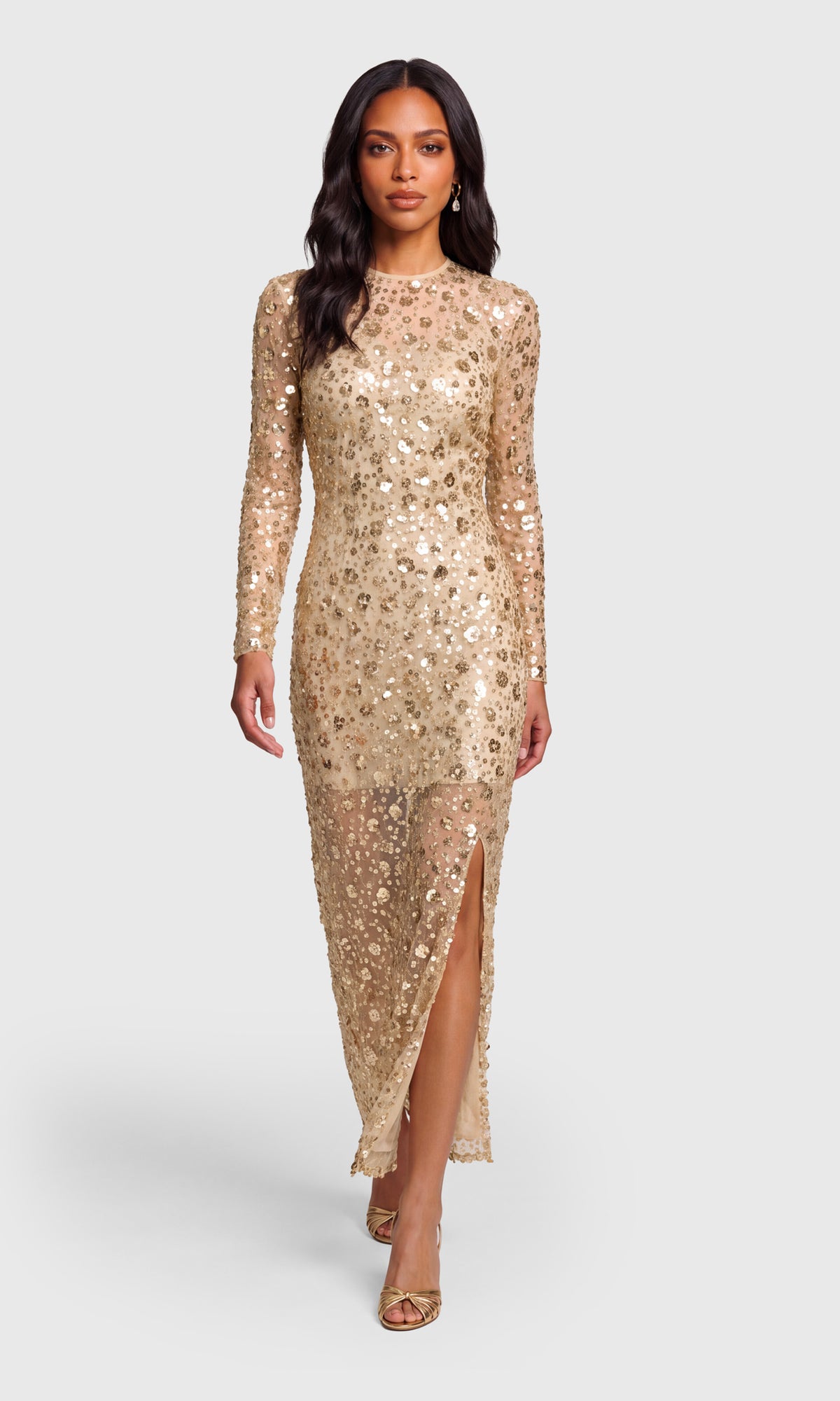 Model wearing a long-sleeve, floor-length champagne gold sequined gown with a thigh-high slit.