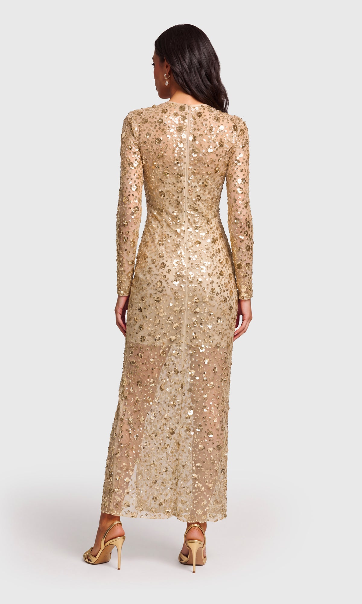 Back view of model wearing a long-sleeve, floor-length champagne gold sequined gown with a thigh-high slit.