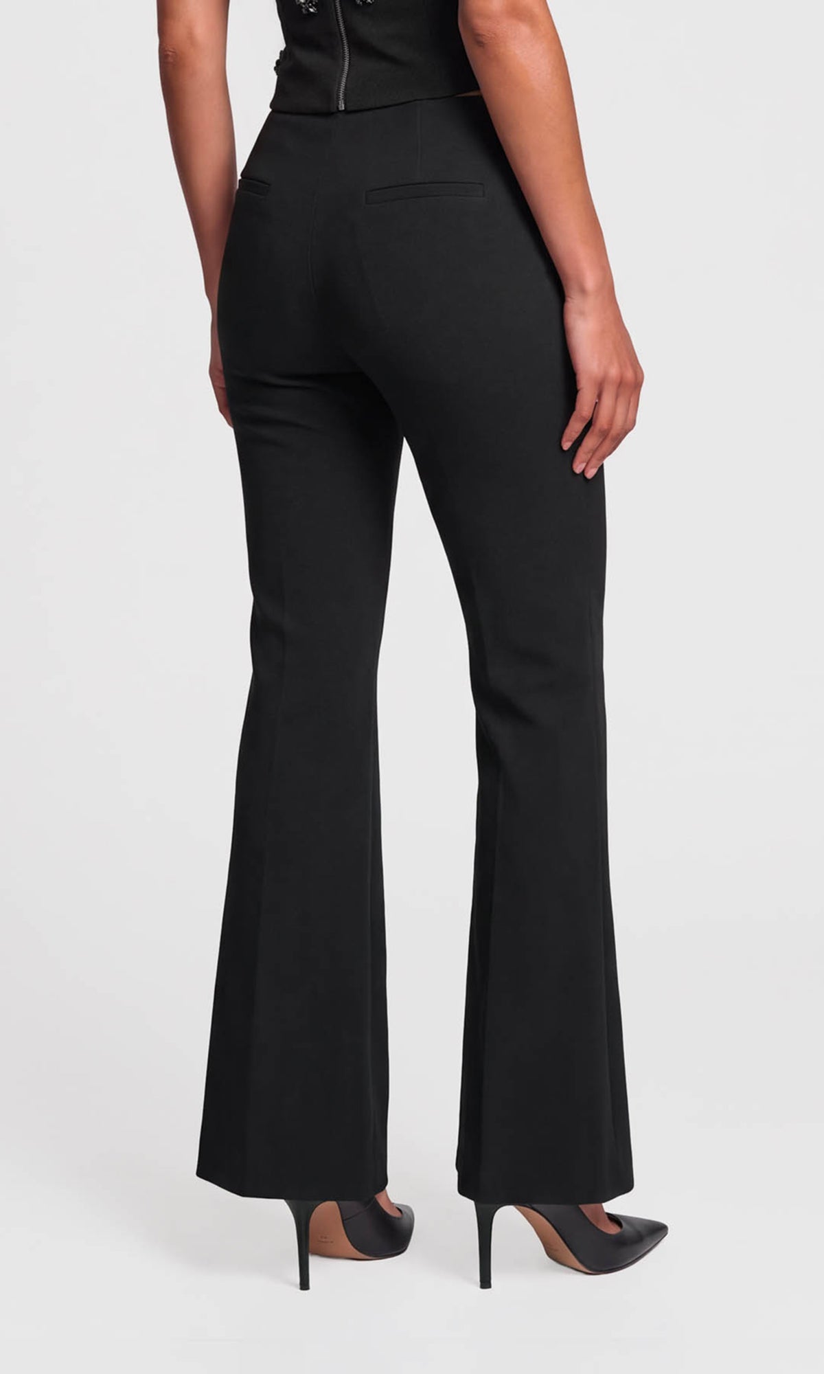 Back view of model wearing black high-waisted flared pants with a straight waistband, paired with black pointed-toe heels.