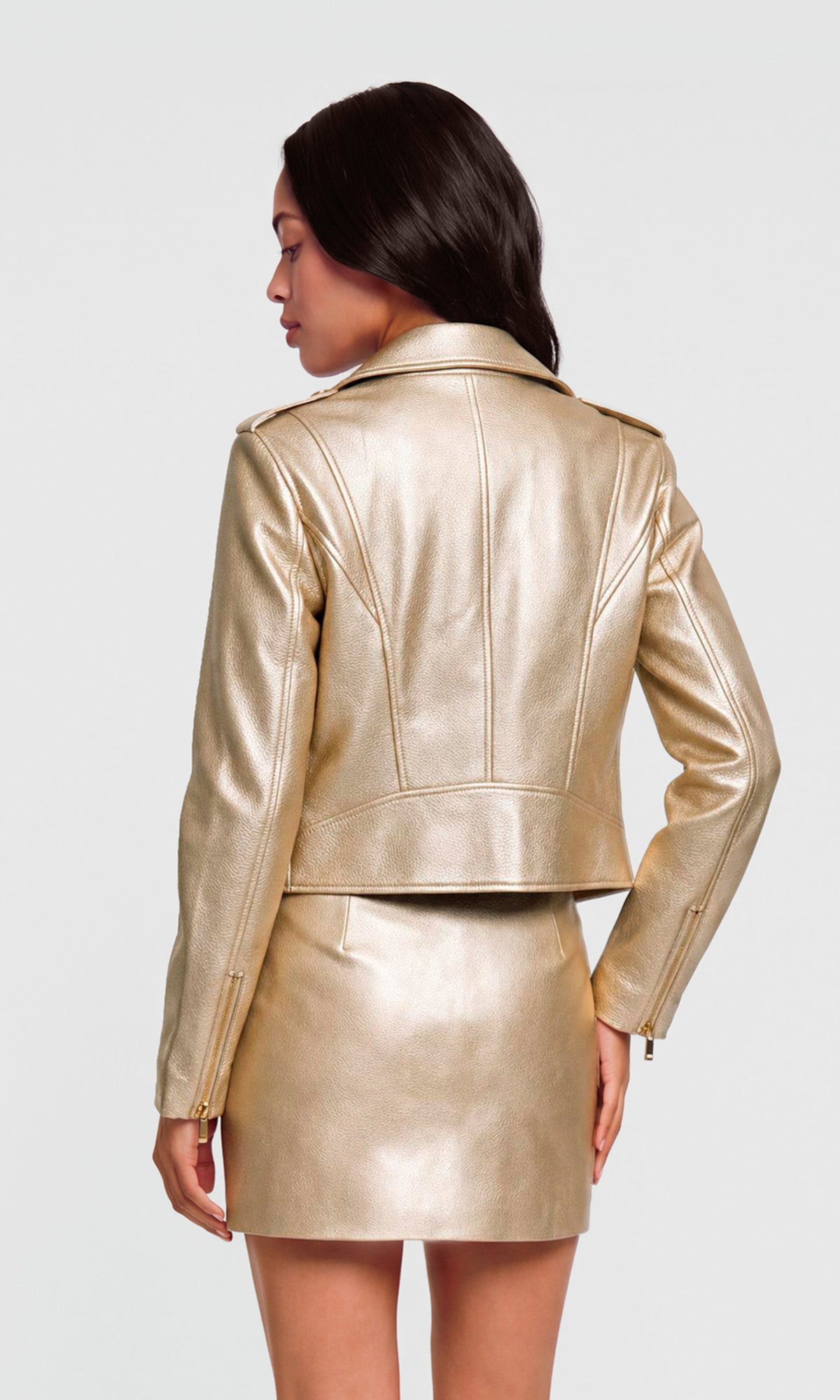 Back view of model wearing a metallic gold faux leather jacket and matching mini skirt.