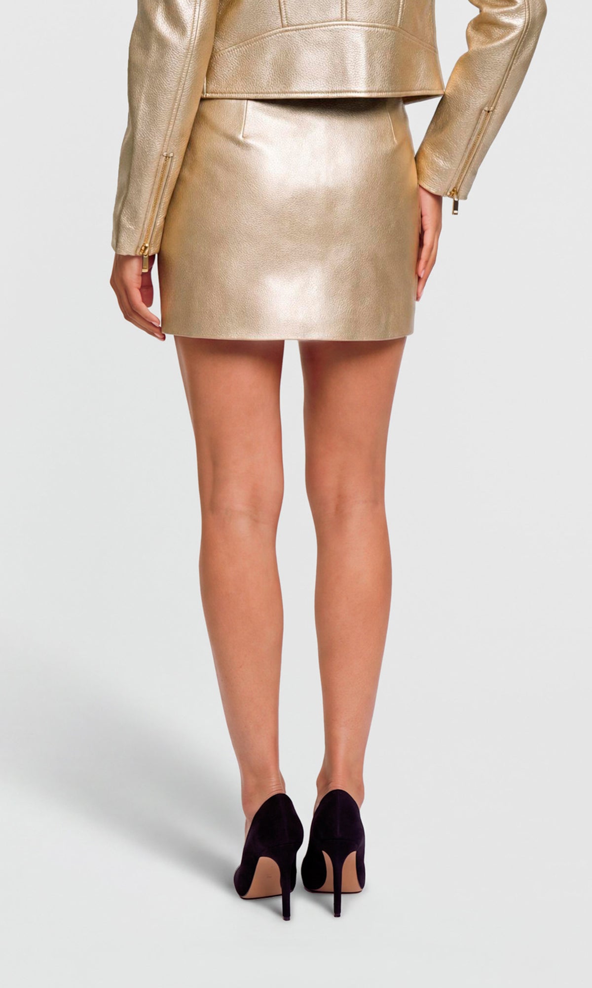 A model shown from the back wearing a metallic gold faux-leather mini skirt with a matching cropped jacket and black high heels.