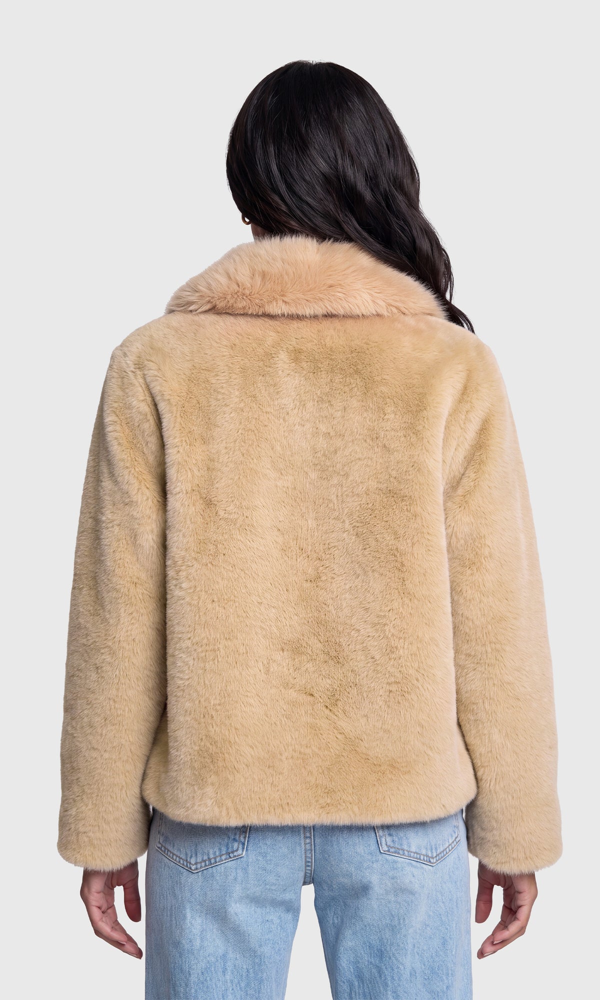 Back view of model wearing a beige fuzzy shearling-style jacket with a wide collar and light blue jeans.