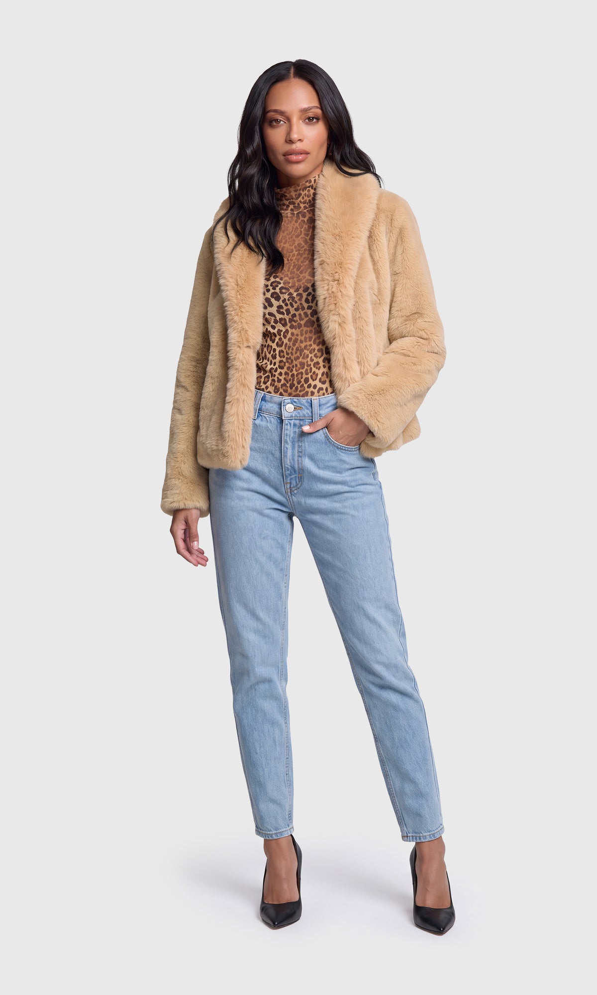 Model wearing a beige faux-shearling jacket over a leopard-print top, paired with light-wash blue jeans and black pointed-toe heels.