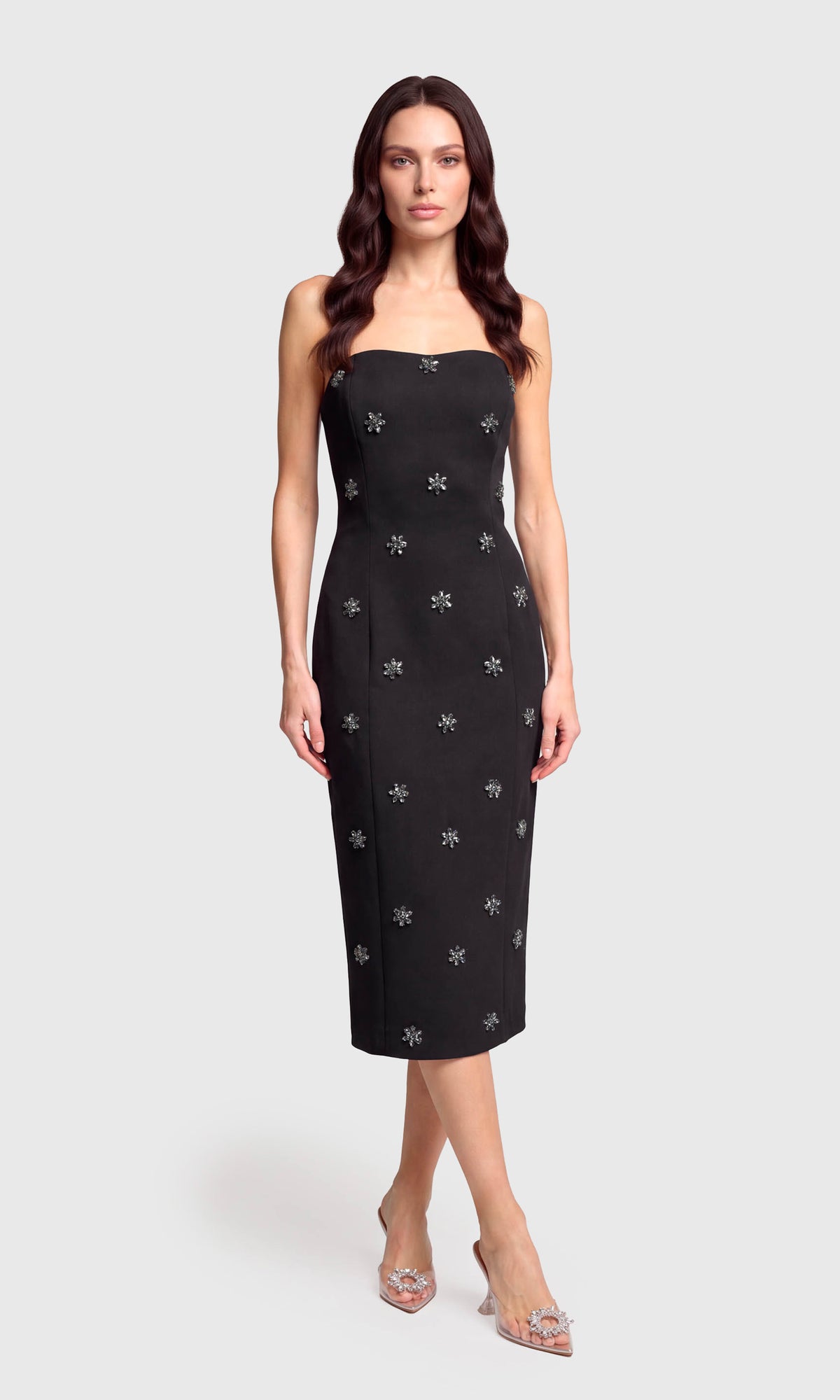 Model wearing a strapless black midi dress with small silver snowflake embroidery, on a plain background.