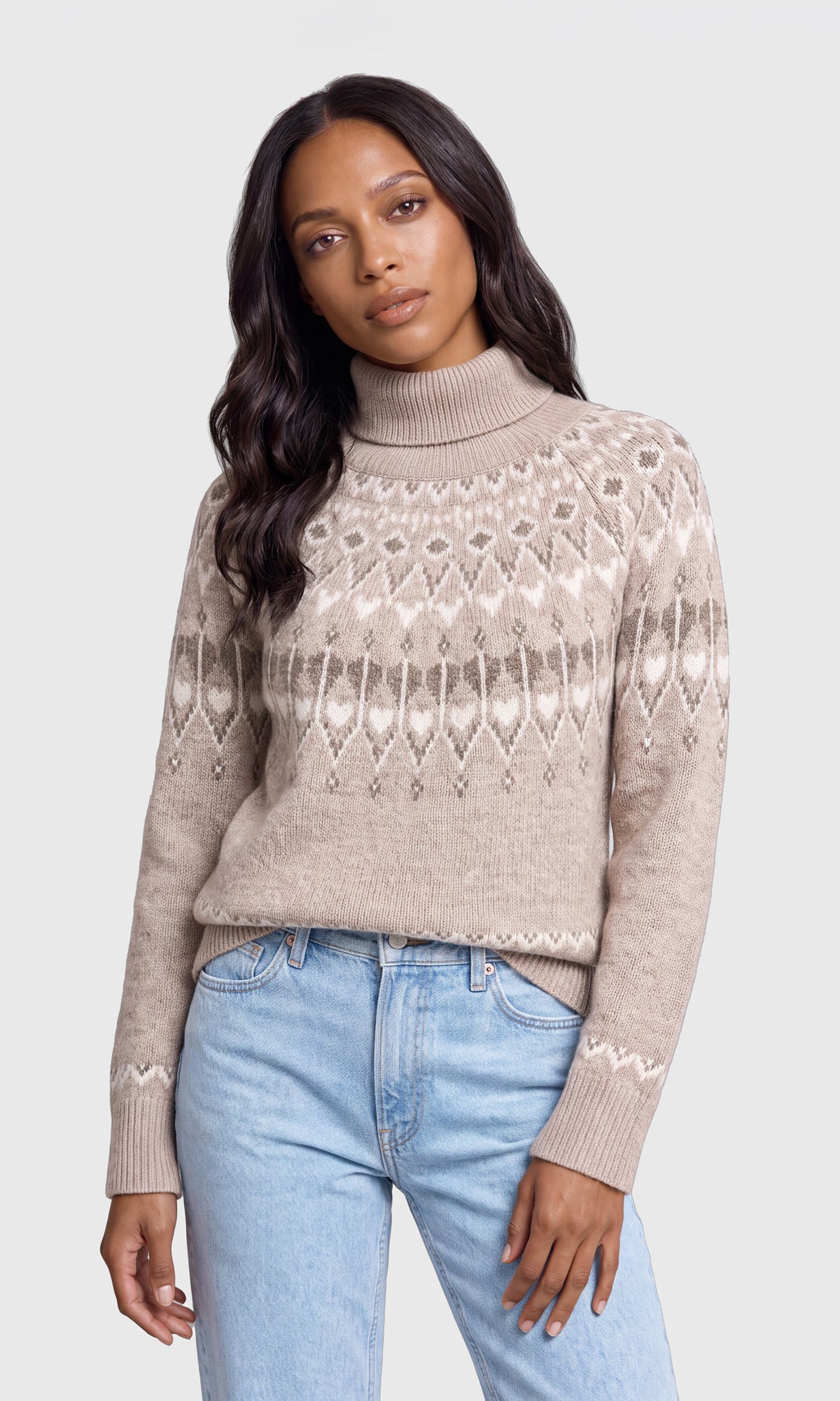 A woman wearing a beige Fair Isle patterned turtleneck sweater and light blue jeans.